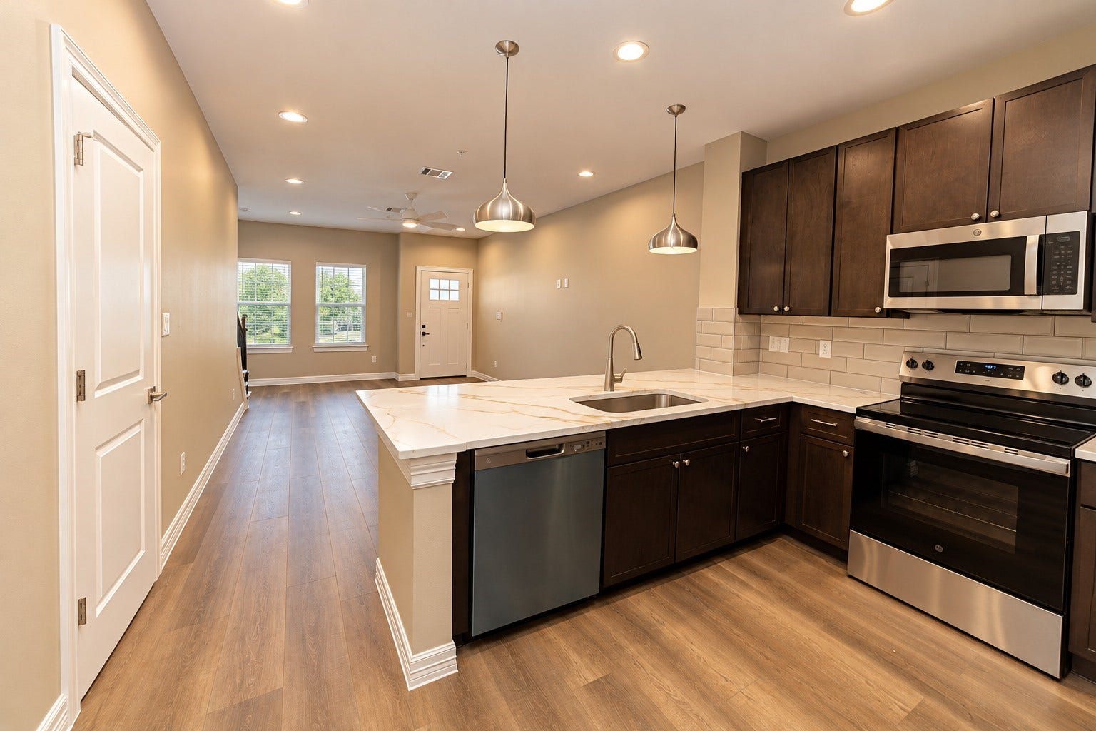 3248 Creekmont Drive, Houston, TX 77091 Modern kitchen with sleek dark cabinetry, stainless steel appliances, and a spacious open-plan layout leading to a bright living area with large windows and vinyl flooring.