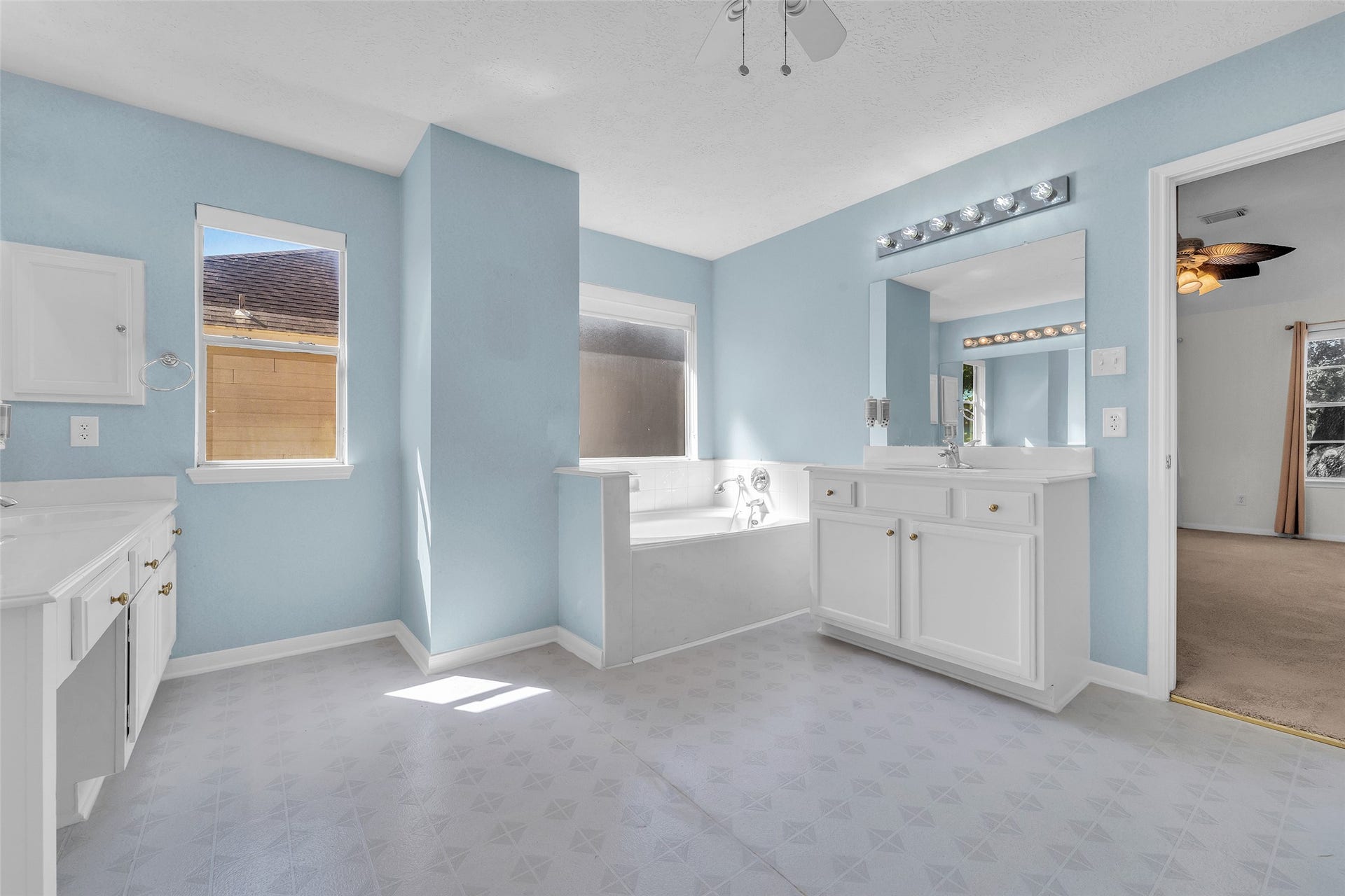 1344 Coleman Boylan Drive, League City, TX 77573 Spacious bathroom with soft blue walls, featuring a large vanity with ample storage, a luxurious soaking tub, and natural light streaming through the window.
