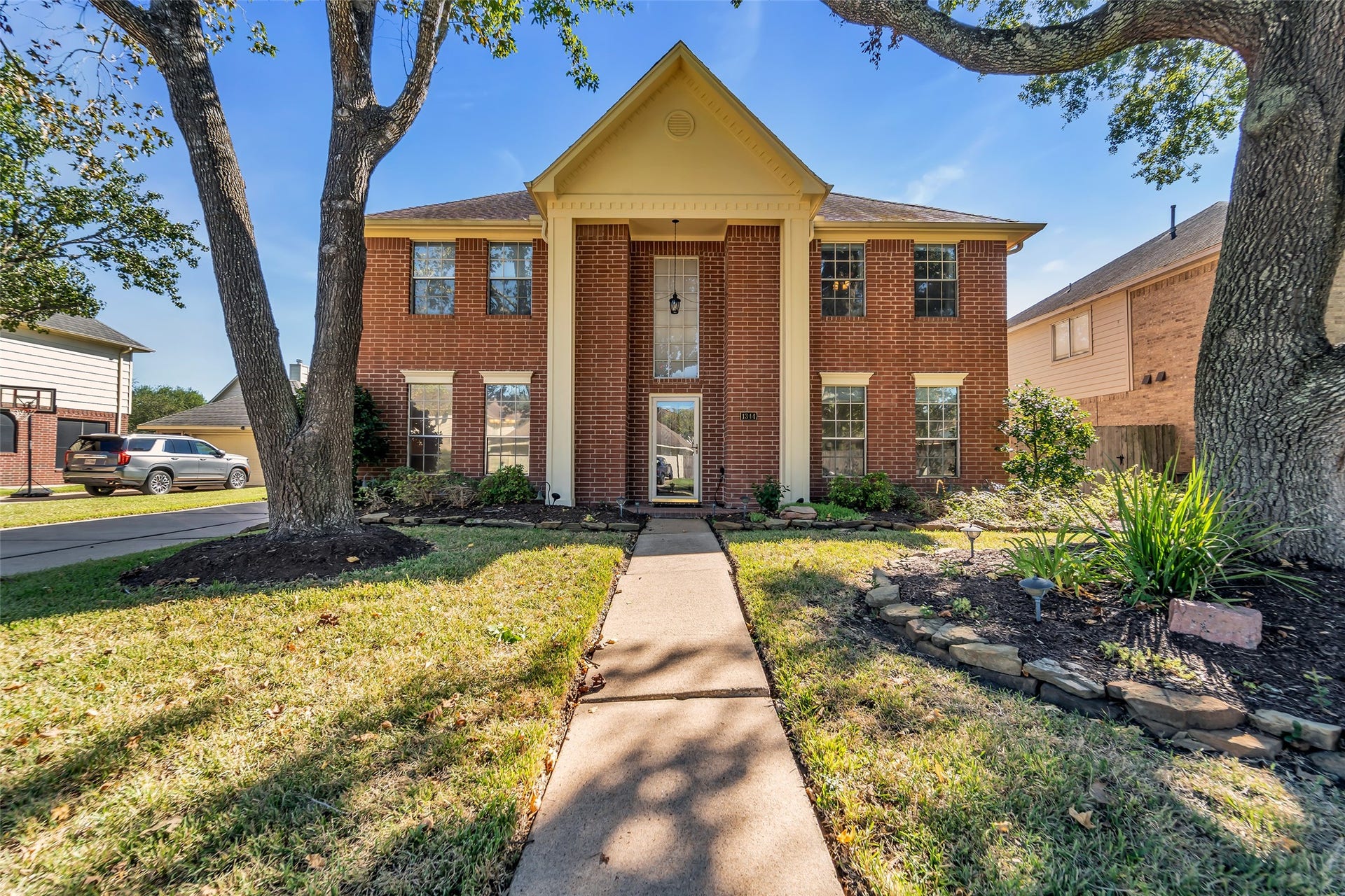 1344 Coleman Boylan Drive, League City, TX 77573 Stately brick home with a grand entrance, framed by mature trees and landscaped gardens, offering charming curb appeal.