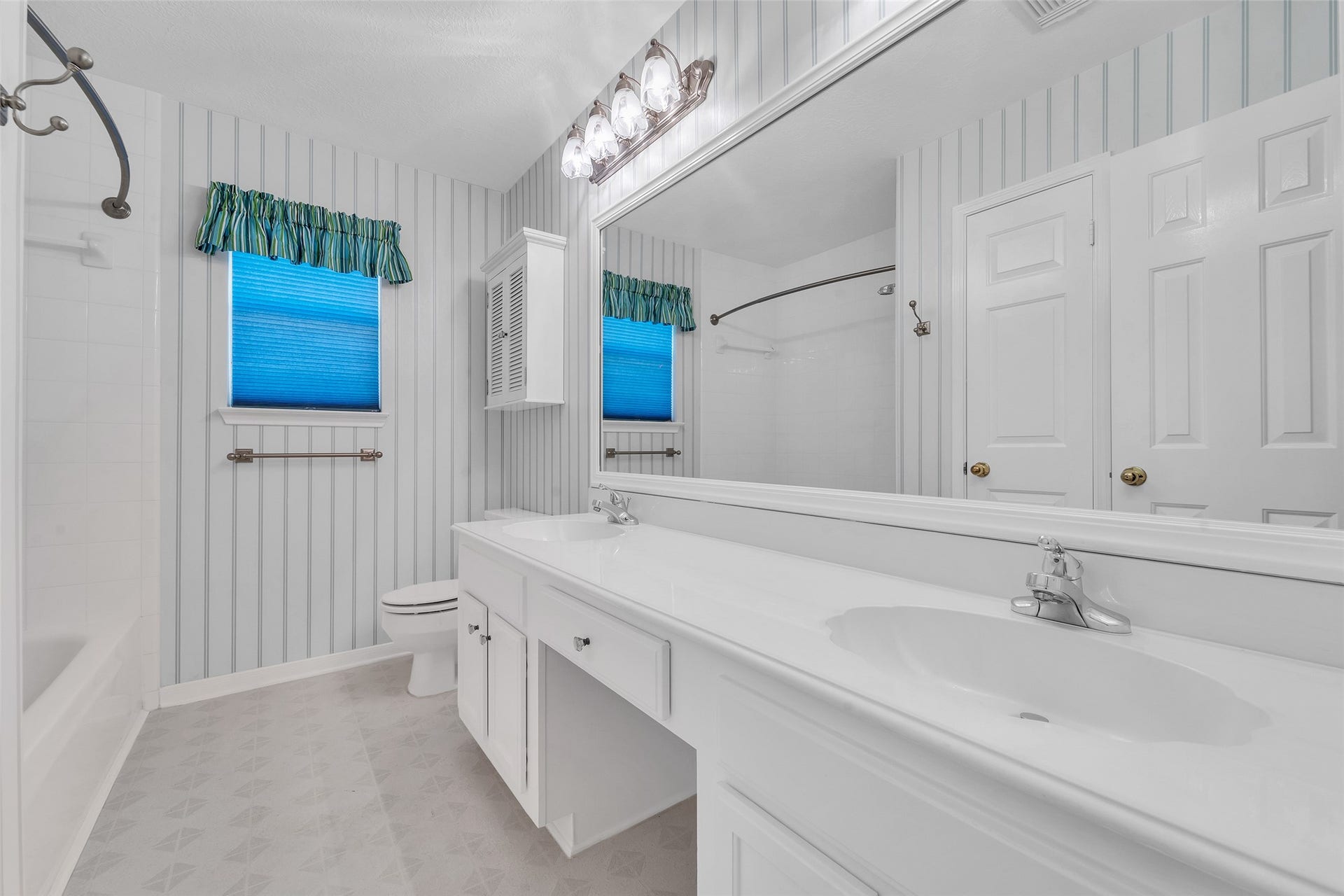 1344 Coleman Boylan Drive, League City, TX 77573 Bright and spacious bathroom featuring a large vanity with double sinks, elegant striped wallpaper, and a combination tub and shower.