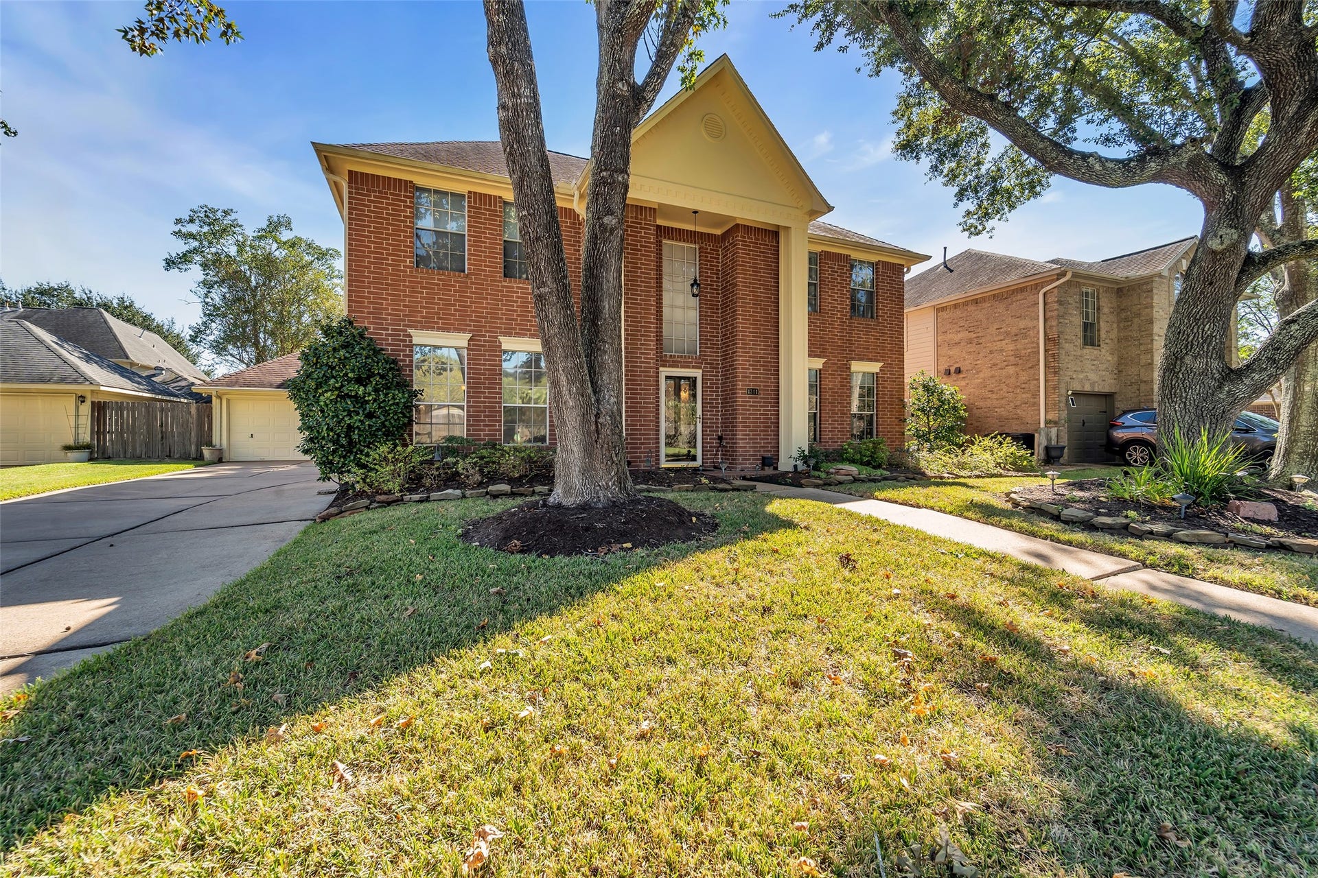 1344 Coleman Boylan Drive, League City, TX 77573 Charming two-story brick home with a welcoming entrance, mature trees, and a spacious driveway leading to a detached garage.