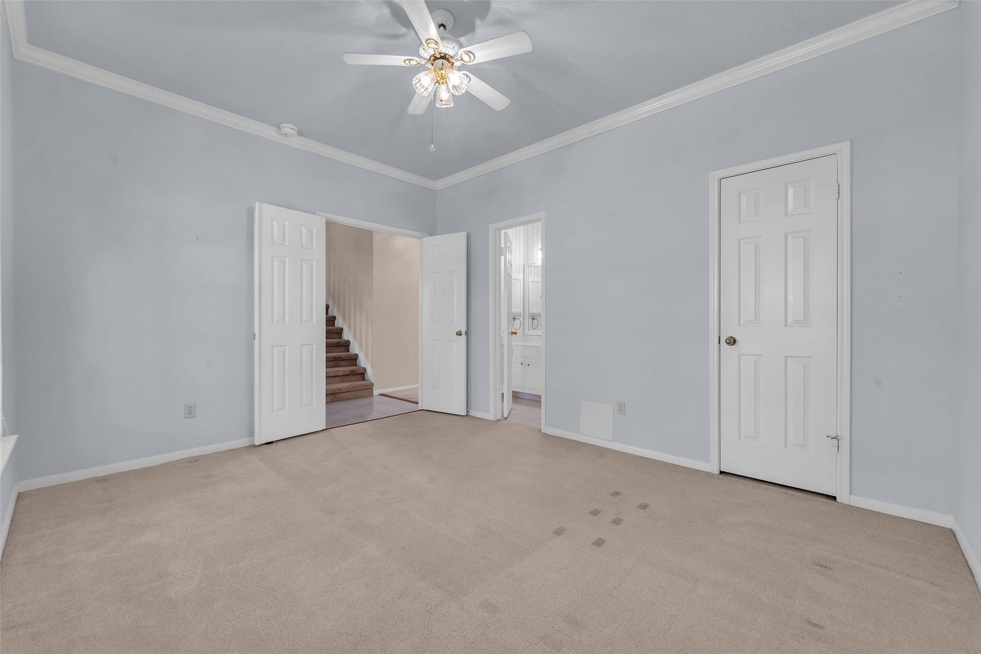 1344 Coleman Boylan Drive, League City, TX 77573 Spacious bedroom with soft blue walls, crown molding, and a ceiling fan, offering access to a bathroom and nearby stairway.
