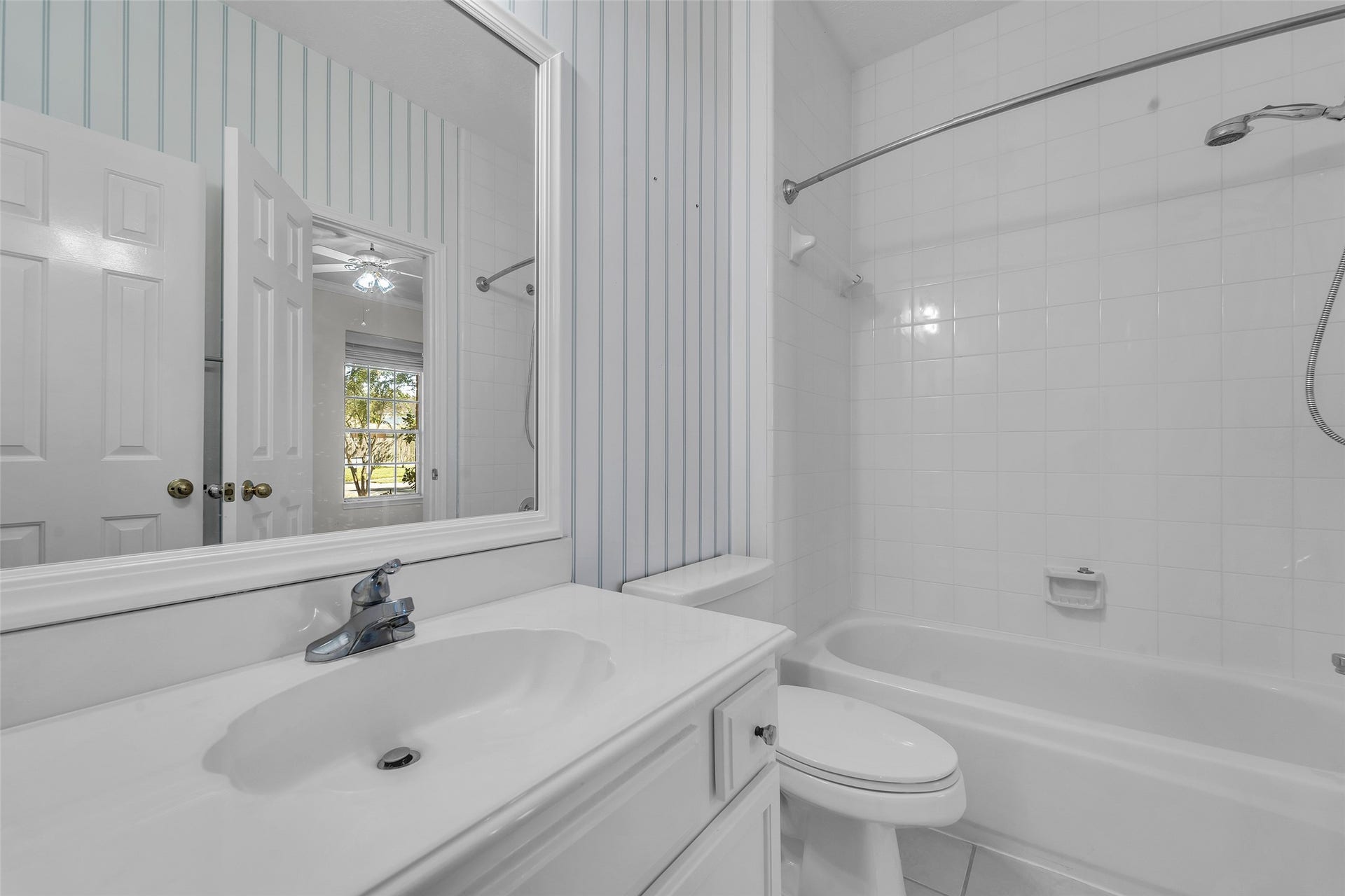 1344 Coleman Boylan Drive, League City, TX 77573 Bright and clean bathroom featuring a classic white tile bathtub, modern sink, and a large mirror with elegant vertical striped wallpaper for a touch of charm.