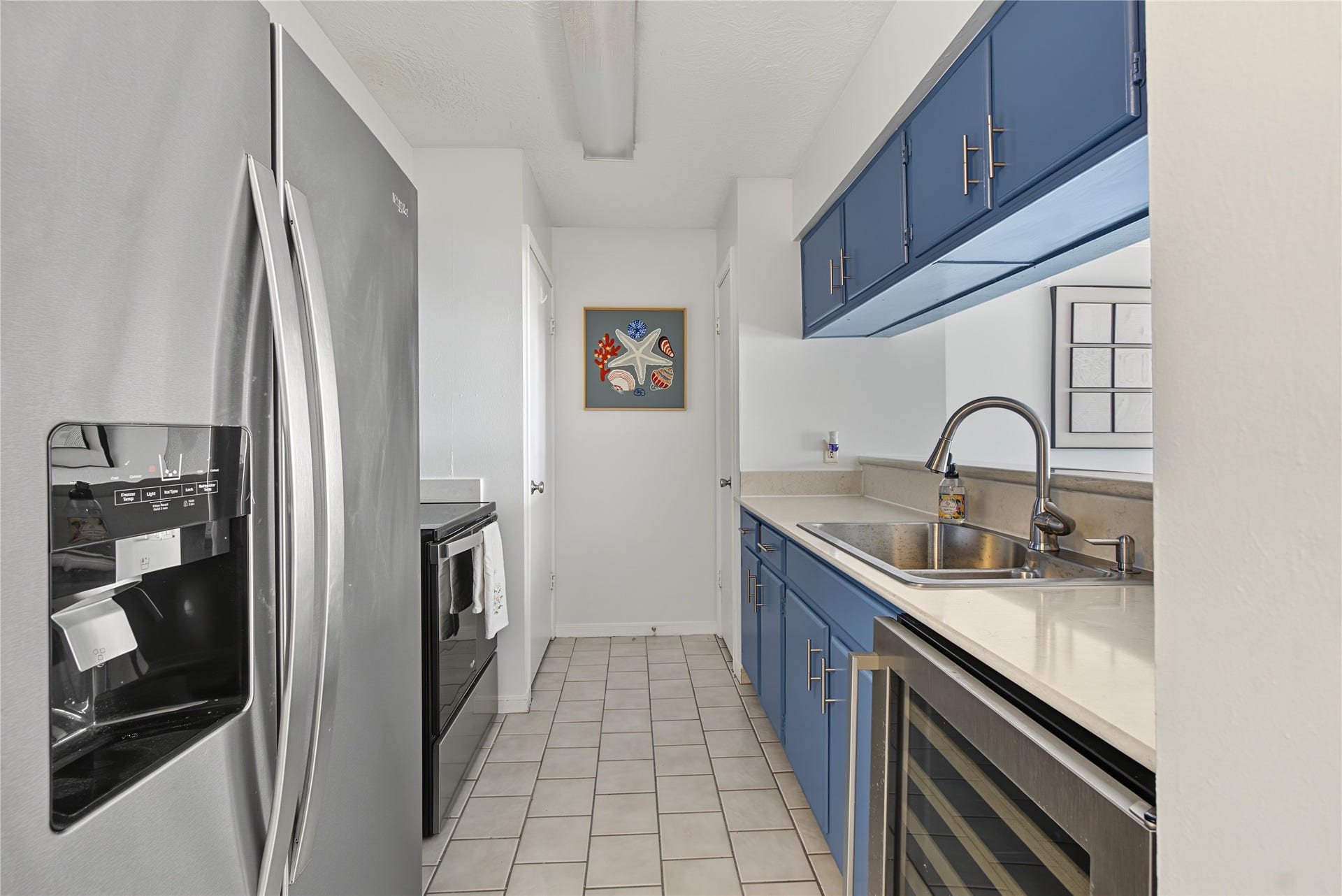 Galley-style kitchen featuring stainless steel appliances, abundant cabinetry, and easy-care tile flooring.