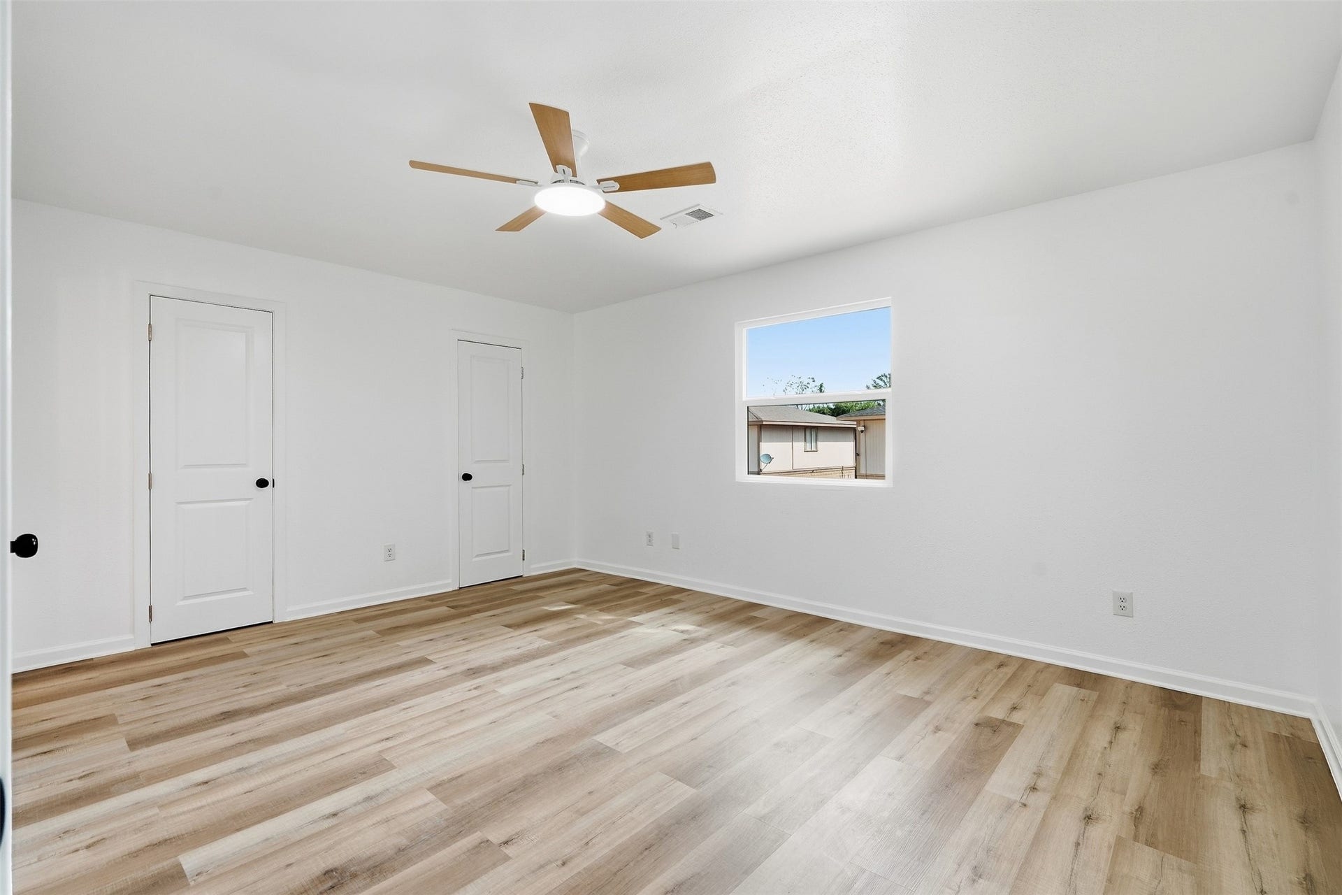 1936 Upland Drive, Houston, TX 77043 Spacious, bright room with modern wood flooring, a ceiling fan, and two closet doors, offering ample natural light through a large window.