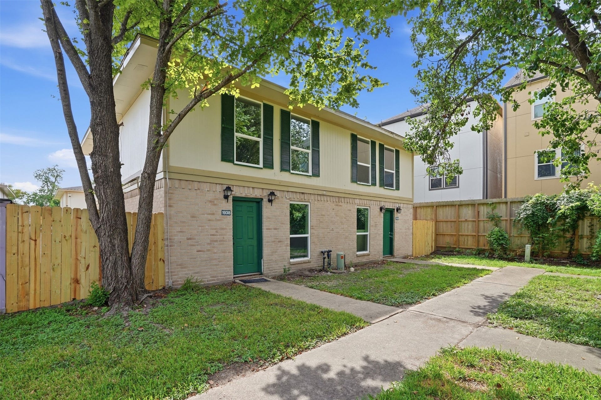 1936 Upland Drive, Houston, TX 77043 Charming two-story home with a brick facade, surrounded by lush greenery and a private fenced yard.