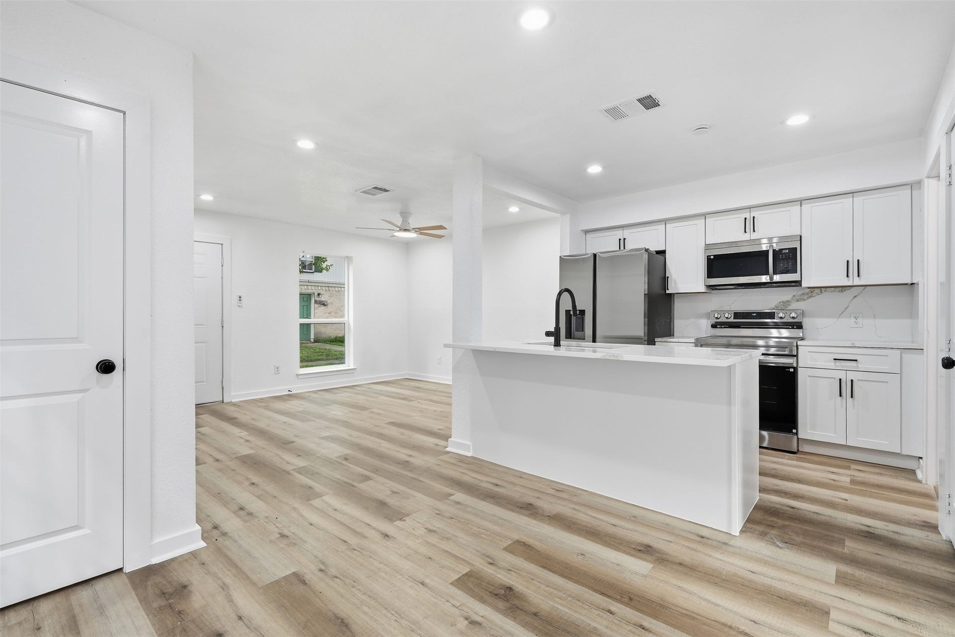 1936 Upland Drive, Houston, TX 77043 Spacious open-concept kitchen and living area featuring sleek white cabinetry, modern appliances, and elegant wood flooring, perfect for entertaining and everyday living.