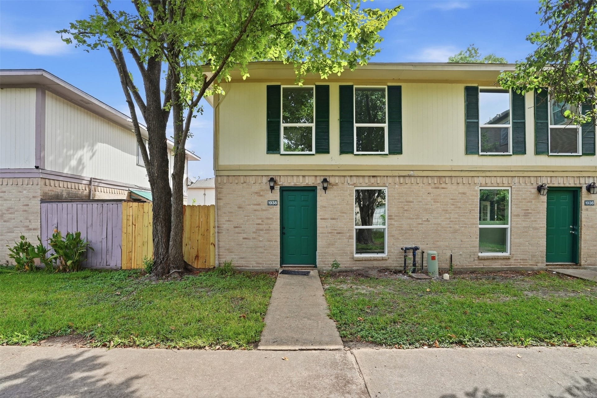 1936 Upland Drive, Houston, TX 77043 Charming two-story townhouse with a warm brick facade and green accents, nestled under mature trees. Features a private entrance and a fenced yard for added privacy.