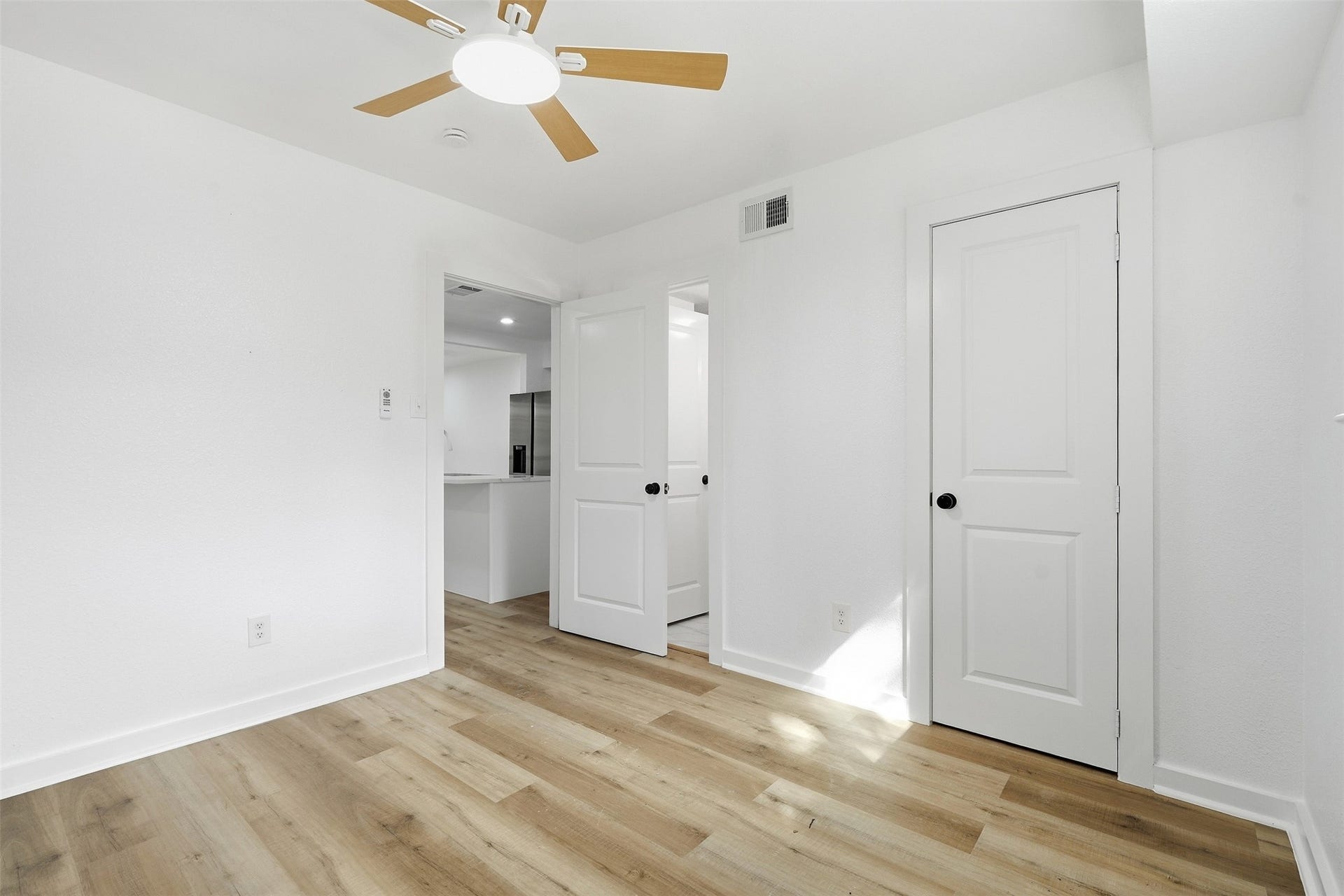 1936 Upland Drive, Houston, TX 77043 Bright and airy room with sleek hardwood floors, modern ceiling fan, and clean white walls. The space offers a glimpse into a stylish, open kitchen, perfect for contemporary living.