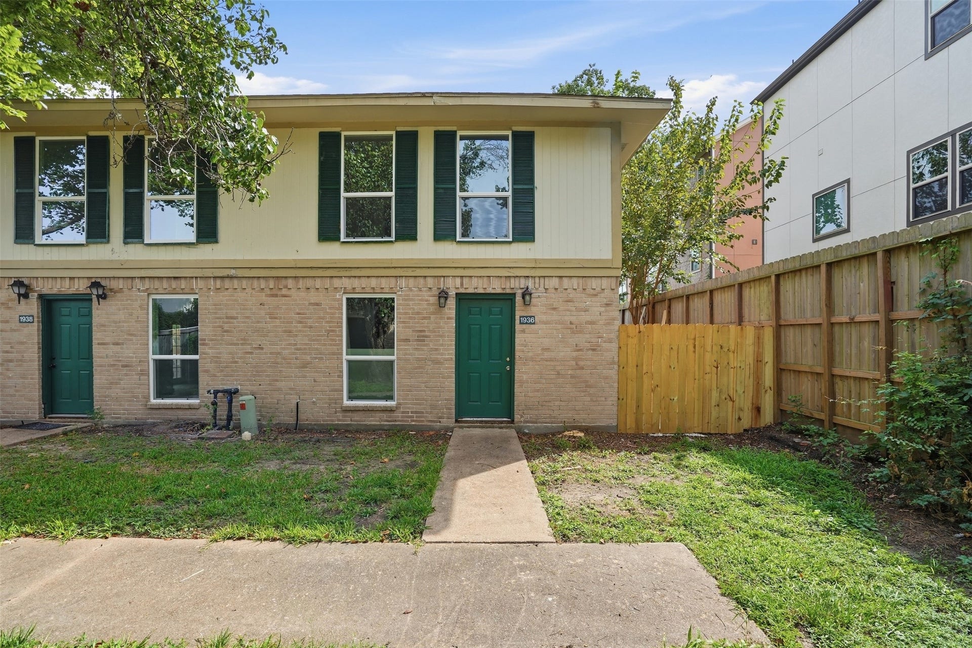 1936 Upland Drive, Houston, TX 77043 Charming end-unit townhouse featuring a classic brick exterior and vibrant green doors, complemented by a cozy fenced side yard.