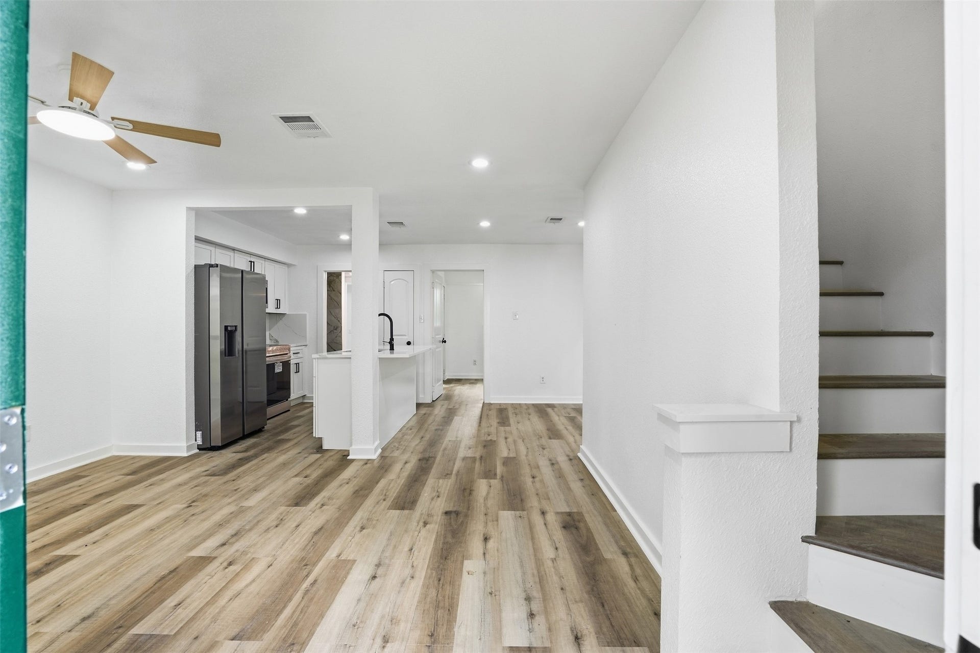 1936 Upland Drive, Houston, TX 77043 Discover a bright, open-concept living space with modern laminate flooring, a sleek ceiling fan, and a stylish kitchen featuring stainless steel appliances and a convenient island. A staircase leads to the upper level, promising additional comfort and space.