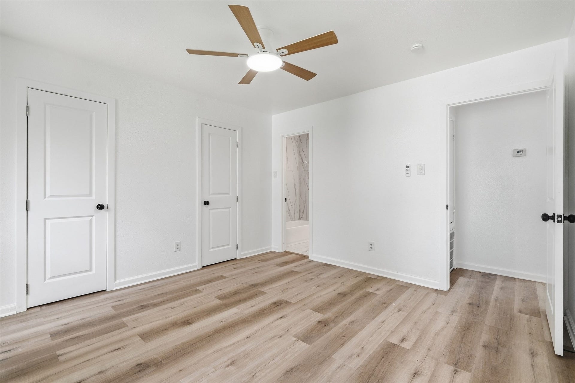 1936 Upland Drive, Houston, TX 77043 Bright and airy bedroom featuring sleek wood flooring, a modern ceiling fan, and convenient access to an elegant bathroom.