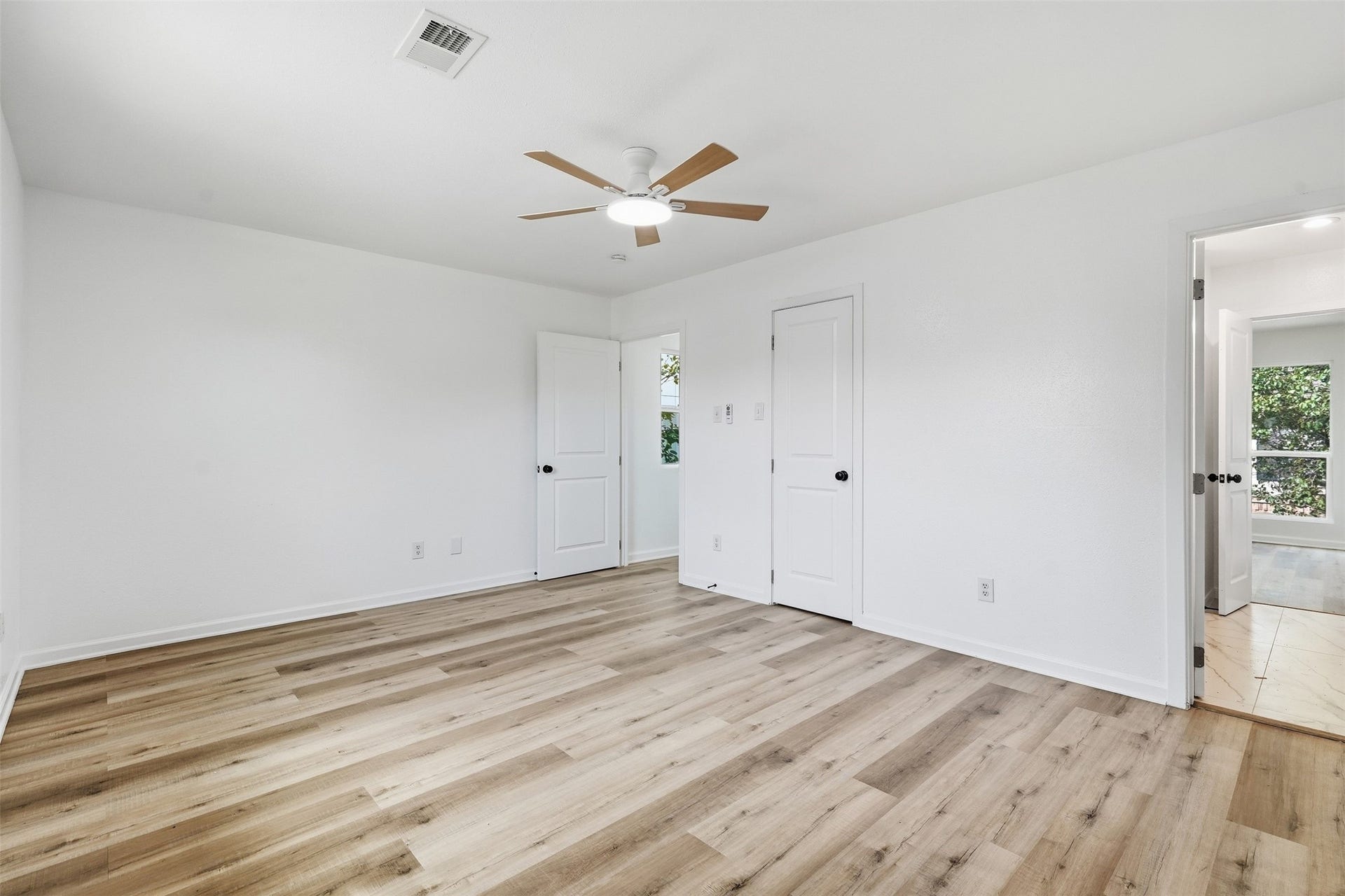 1936 Upland Drive, Houston, TX 77043 Bright and spacious bedroom featuring sleek hardwood floors, a modern ceiling fan, and ample natural light streaming through the windows.
