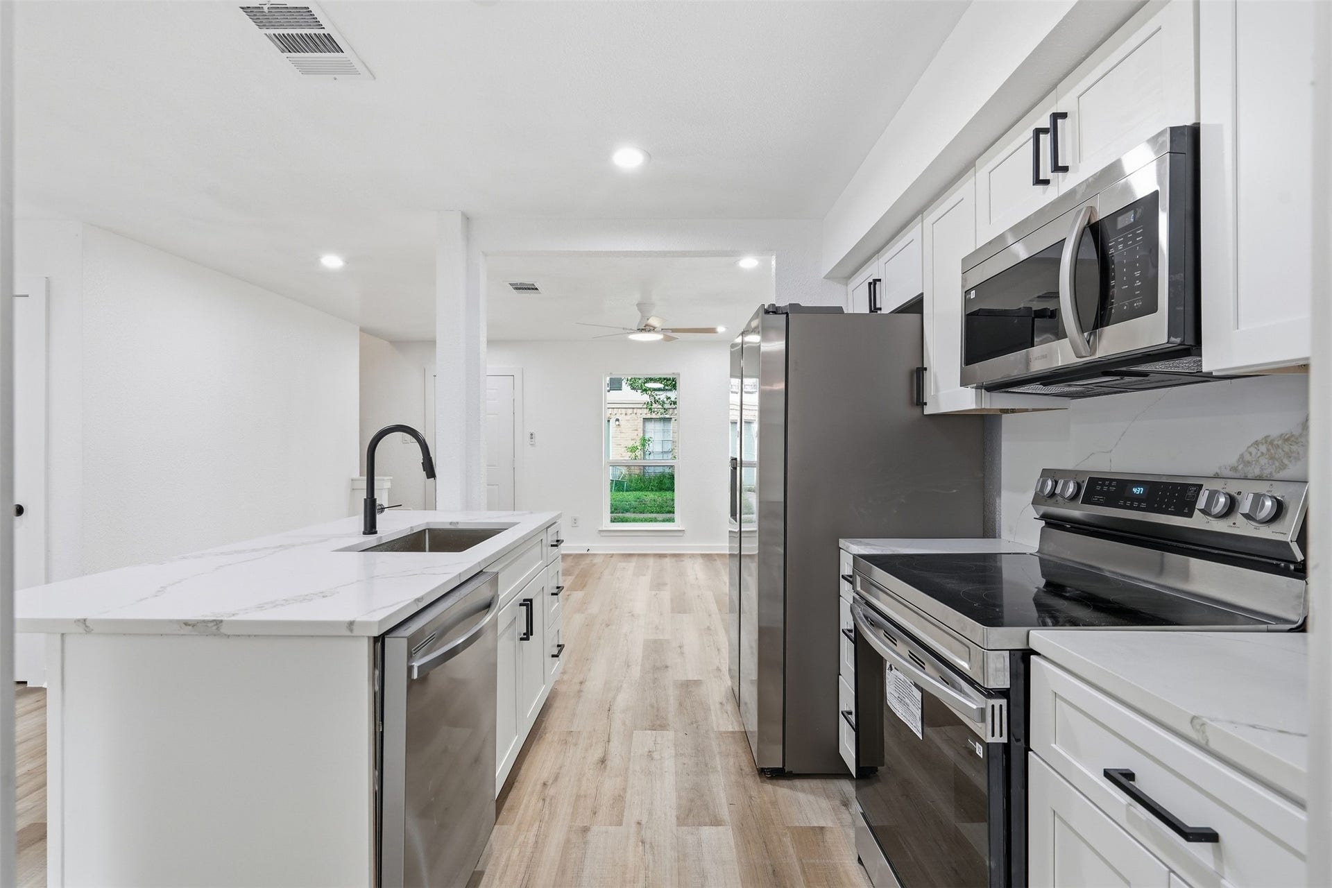 1936 Upland Drive, Houston, TX 77043 Modern kitchen featuring sleek stainless steel appliances, elegant white cabinetry, and a spacious island with a marble countertop, seamlessly flowing into the open living area with abundant natural light.