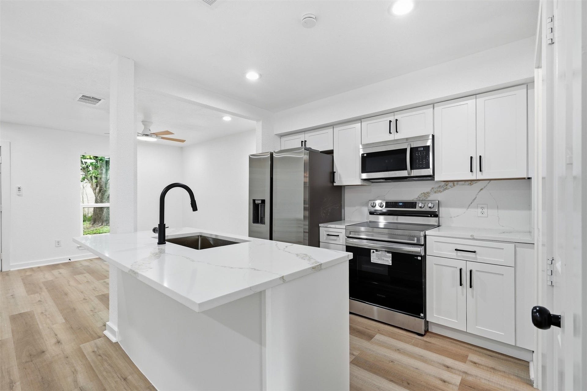 1936 Upland Drive, Houston, TX 77043 Sleek modern kitchen with stainless steel appliances, white cabinetry, and a spacious island featuring a black faucet.