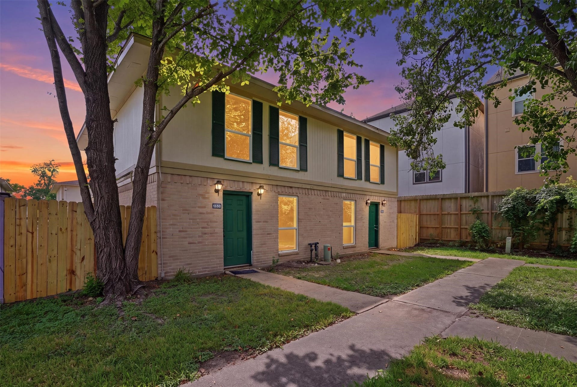 1936 Upland Drive, Houston, TX 77043 Charming two-story home with a warm brick exterior, green shutters, and a welcoming front yard, nestled under mature trees and set against a picturesque sunset backdrop.