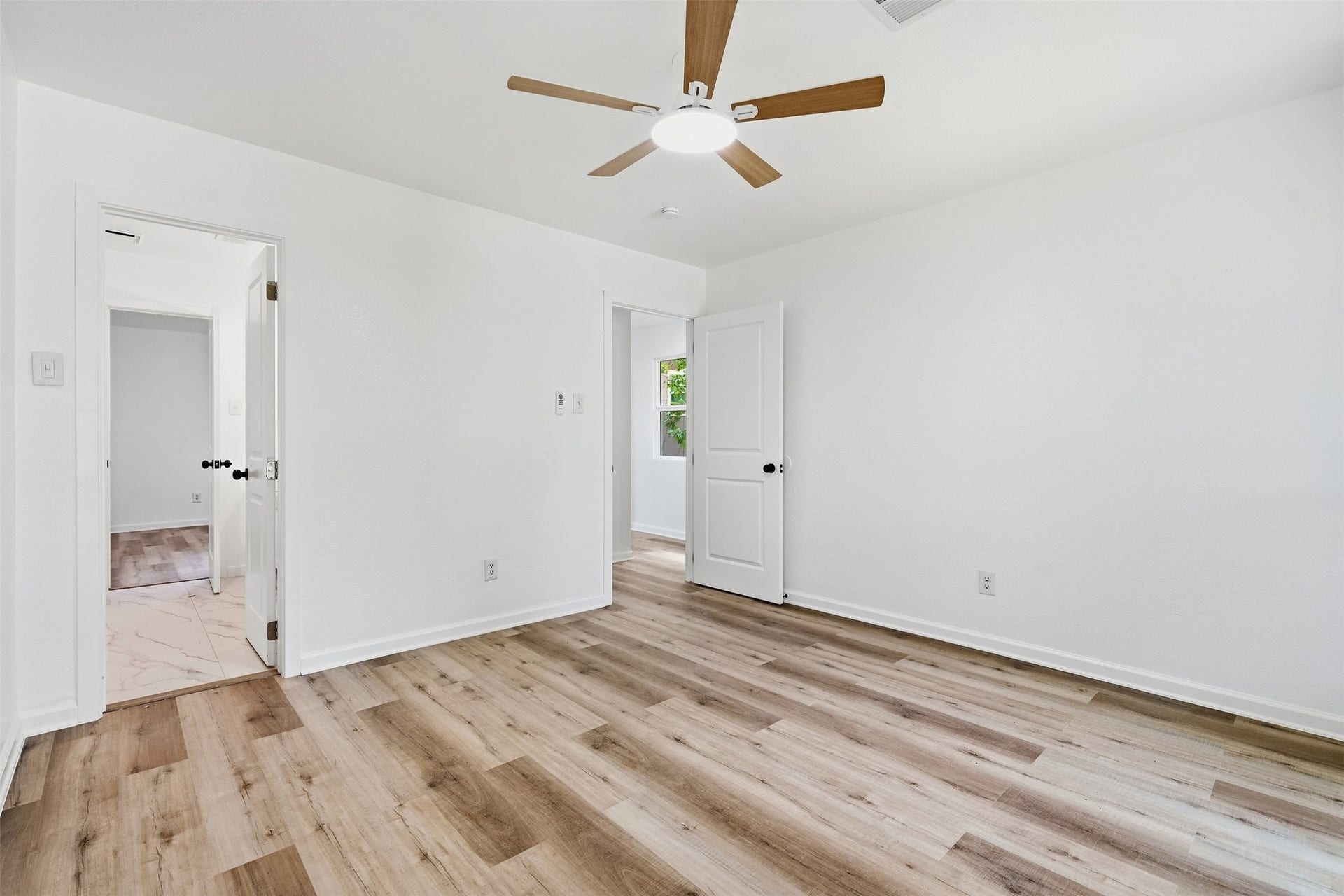 1936 Upland Drive, Houston, TX 77043 Bright and airy bedroom featuring sleek wood flooring, neutral walls, and a modern ceiling fan, with easy access to connecting rooms.