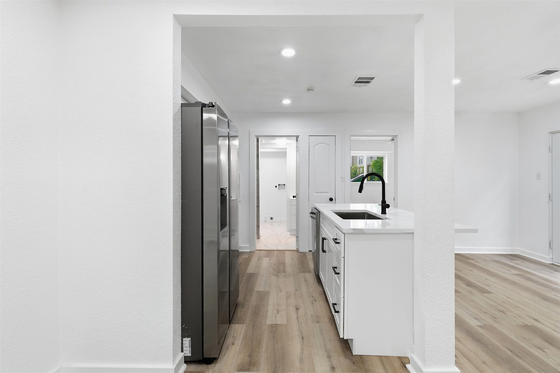 1936 Upland Drive, Houston, TX 77043 Sleek modern kitchen with white cabinetry, a stylish black faucet, and stainless steel appliances, complemented by light wood flooring.