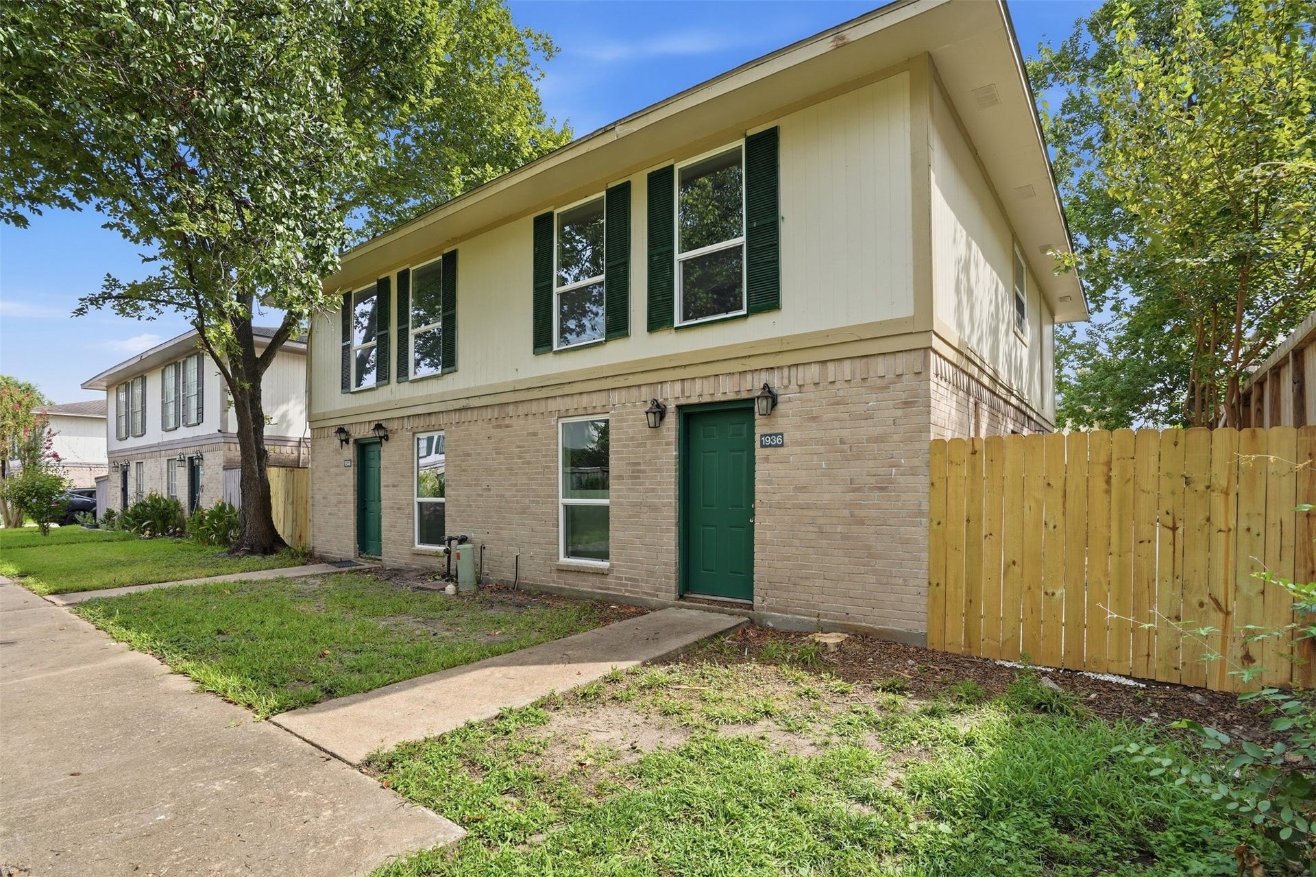 1936 Upland Drive, Houston, TX 77043 Charming two-story home with a brick facade, featuring large windows and a welcoming green front door. The property is complemented by a well-maintained lawn and a wooden privacy fence.