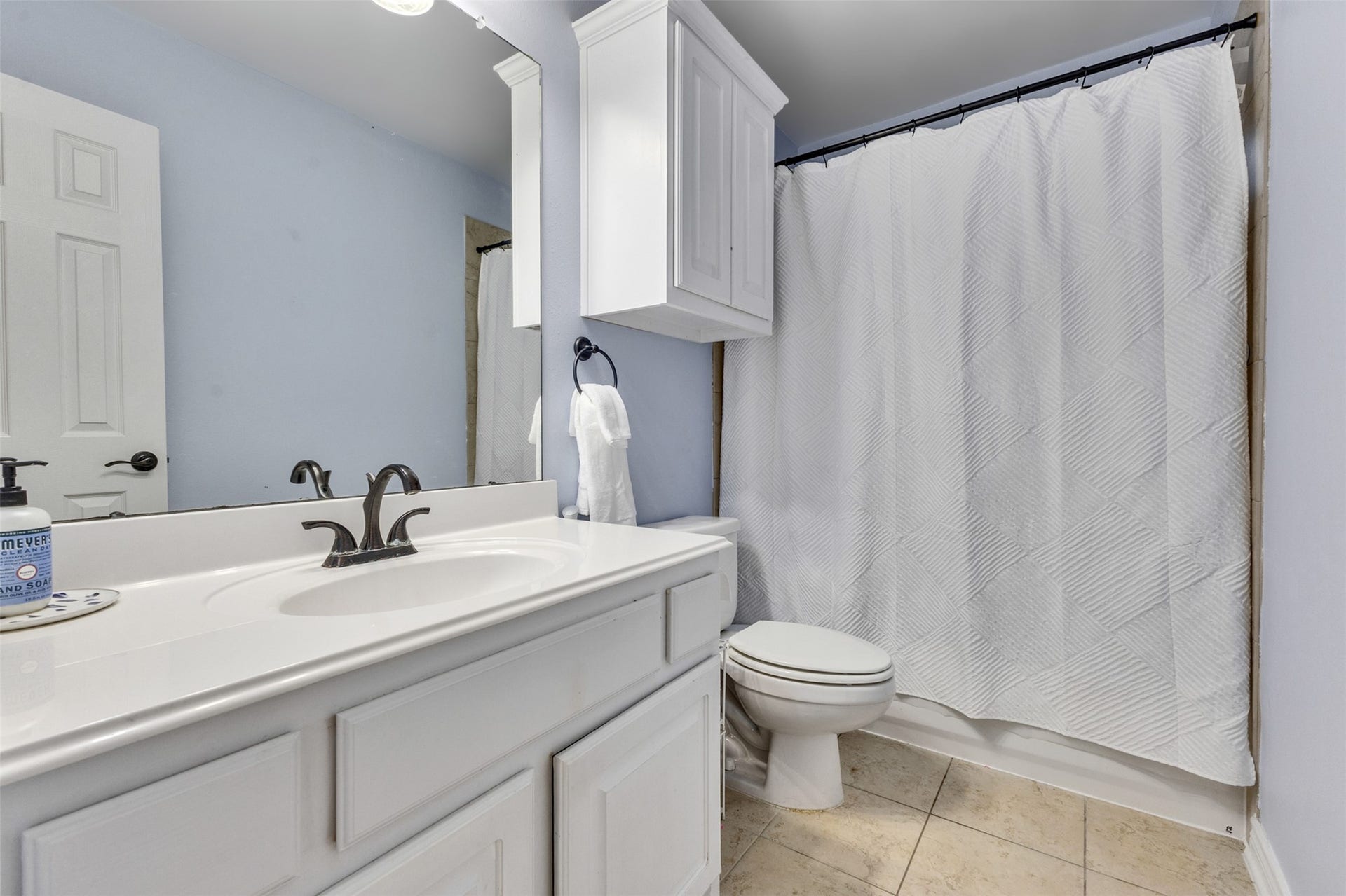 A bright, functional bathroom featuring a tub/shower combination, white cabinetry, and additional storage for everyday essentials.