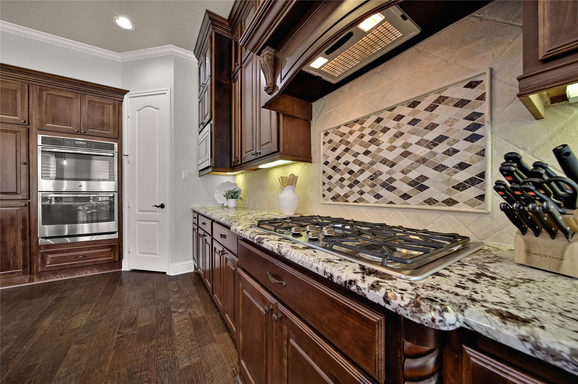27707 Lakeway Trail Lane, Fulshear, TX 77441 The kitchen boasts exotic granite countertops and tumbled travertine backsplashes, highlighted by a stunning mosaic design above the cooktop that adds a unique touch of elegance and character.