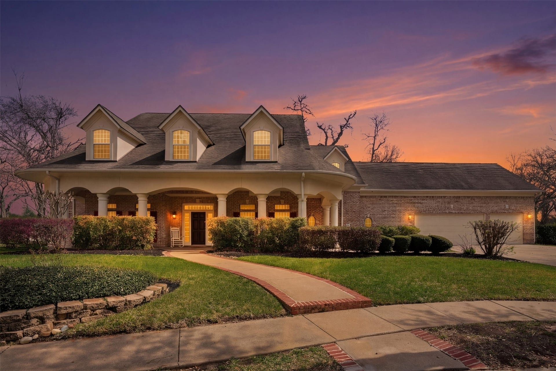 3 Wilmington Court, Sugar Land, TX 77479 Charming two-story home with inviting front porch, dormer windows, and beautifully manicured landscaping, set against a stunning sunset backdrop.