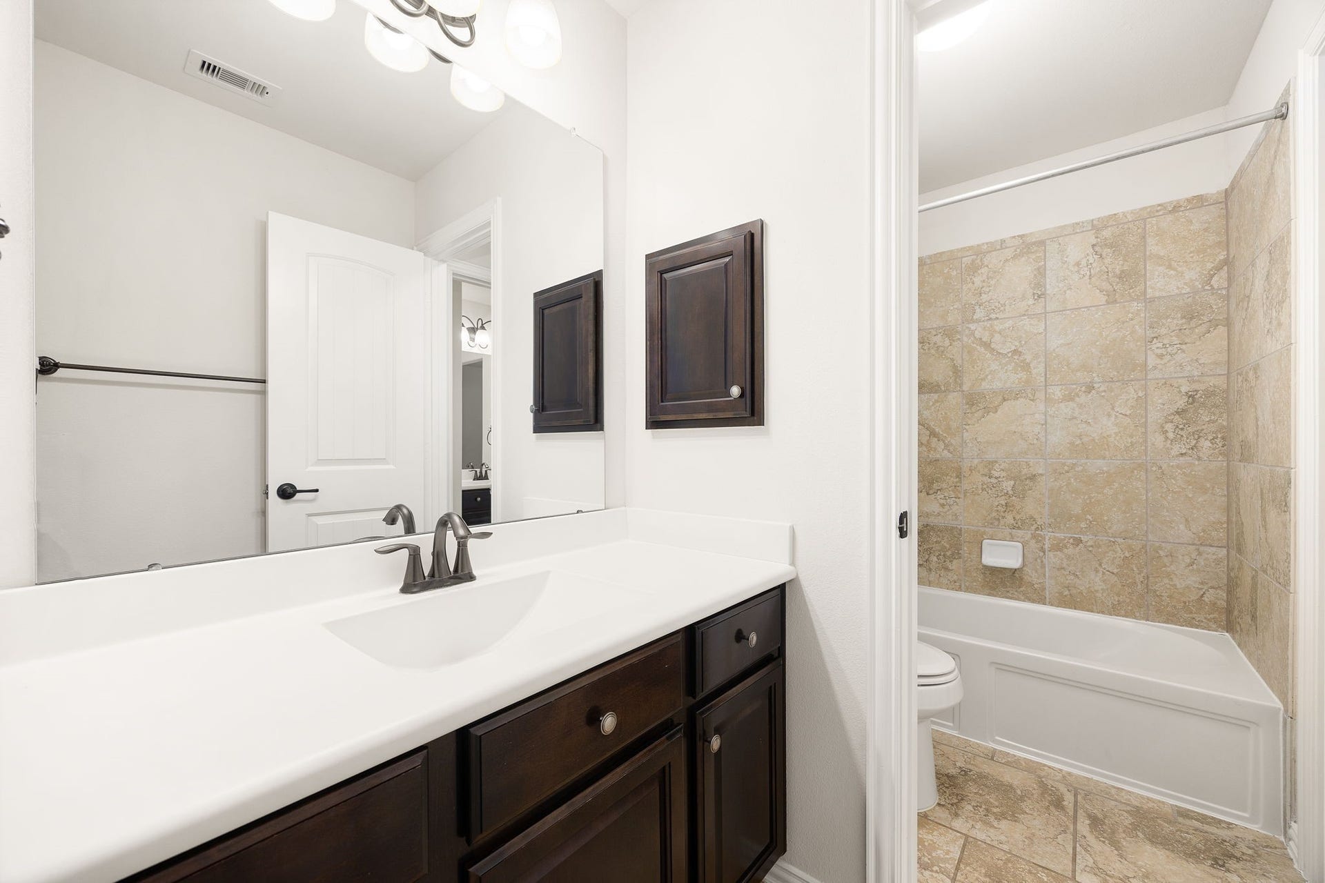 9931 Hutton Park Drive, Katy, TX 77494 This secondary bathroom serves as one half of the convenient shared Jack-and-Jill layout, complete with its own private vanity area. The space features a rich dark wood vanity with a crisp white countertop and modern oil-rubbed bronze plumbing fixtures, which seamlessly flows into a separate toilet and a beautifully tiled tub-and-shower combination.
