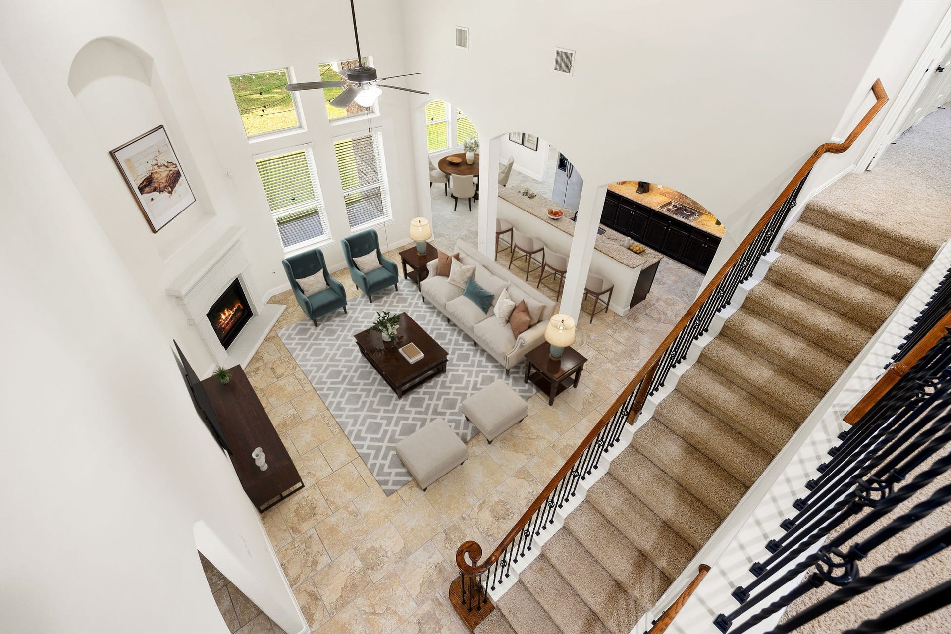 9931 Hutton Park Drive, Katy, TX 77494 Looking down from the upper gallery landing, this perspective showcases the grand proportions of the double-height great room. The sweeping staircase frames the view, revealing the seamless transition between the light-filled main living space, the classic fireplace hearth, and the spacious tile flooring below.