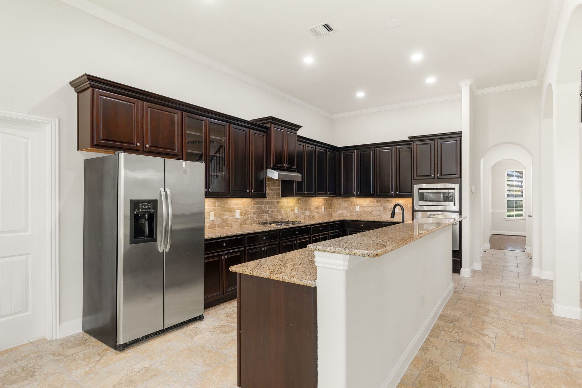 9931 Hutton Park Drive, Katy, TX 77494 This gourmet kitchen features stunning dark wood cabinetry, expansive granite countertops, and premium stainless steel appliances. An oversized island offers additional workspace and a breakfast bar, while the under-cabinet lighting perfectly illuminates the sleek tile backsplash. With its open layout flowing into the rest of the home and recessed ceiling lights, this space is ideal for both everyday living and hosting.