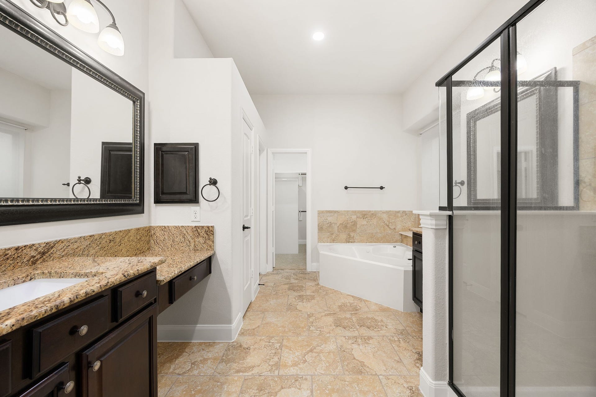 9931 Hutton Park Drive, Katy, TX 77494 The spa-like primary bathroom serves as a luxurious retreat, featuring an expansive dual-sink vanity with a dedicated makeup station. This beautifully designed layout includes a deep soaking tub, a separate glass-enclosed shower with a modern dark frame, and elegant stone countertops that match the home's cohesive design.