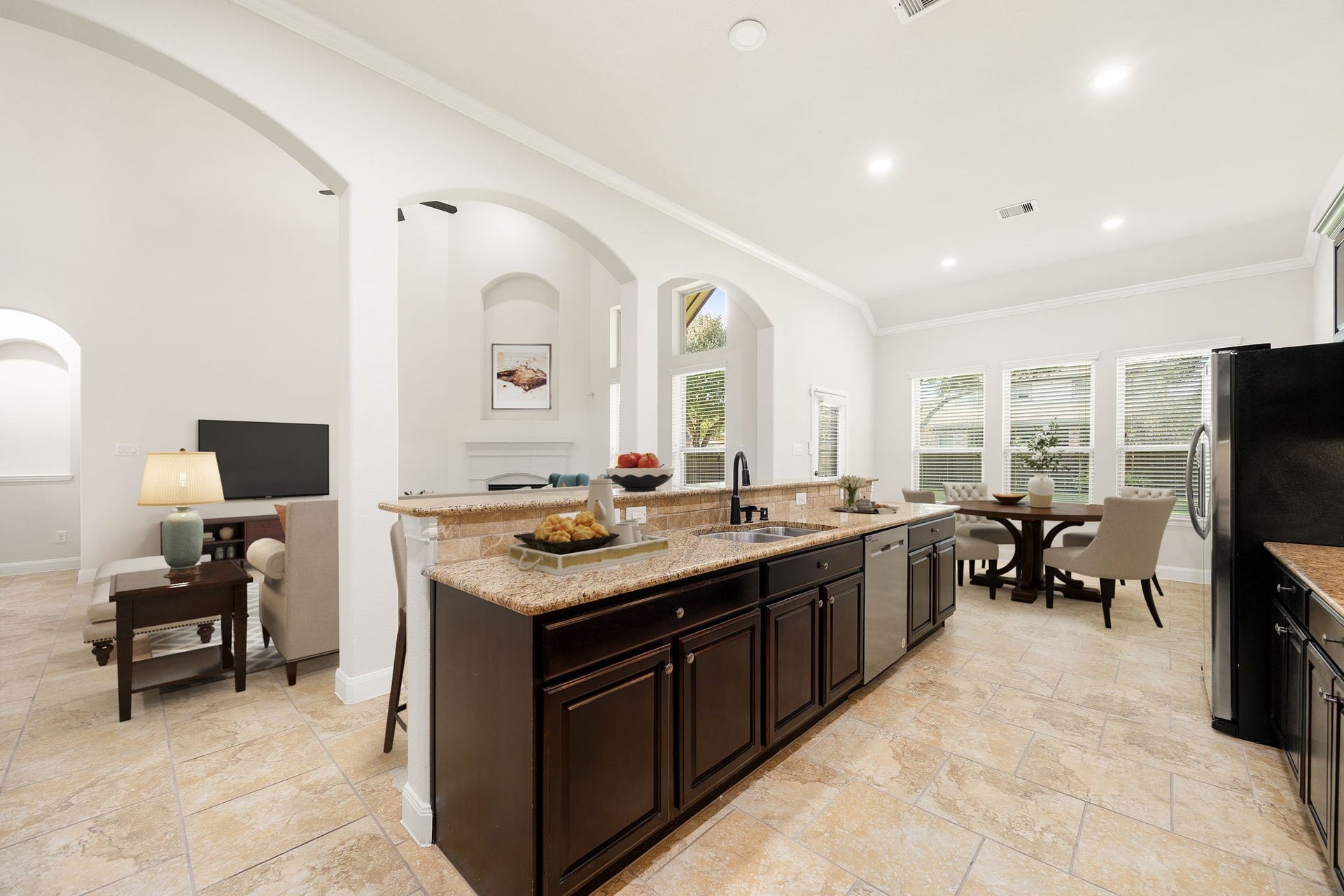 9931 Hutton Park Drive, Katy, TX 77494 This spacious kitchen features an expansive multi-level island with a built-in sink and an extended breakfast bar that overlooks the primary living areas. Timeless architectural arches frame the space, which boasts dark custom cabinetry, stainless steel appliances, and a bright breakfast nook situated right next to a wall of windows.