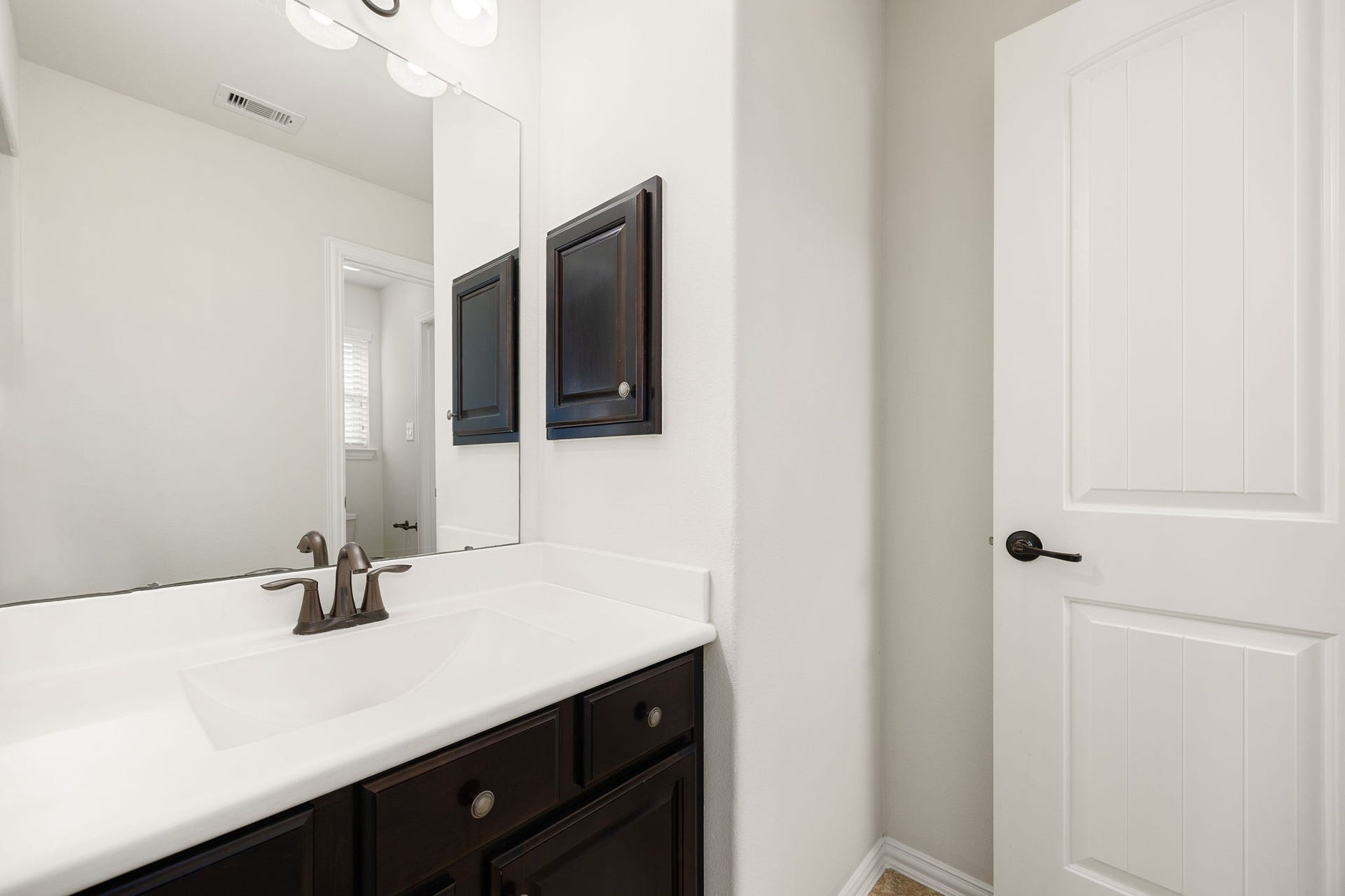 9931 Hutton Park Drive, Katy, TX 77494 This view highlights the matching secondary vanity station connected to the opposite bedroom of the functional Jack-and-Jill layout. Mirroring the high-end finishes of the first side, it features its own independent grooming space with a rich dark wood cabinet, a clean white countertop, and oil-rubbed bronze accents to ensure individual privacy and convenience.