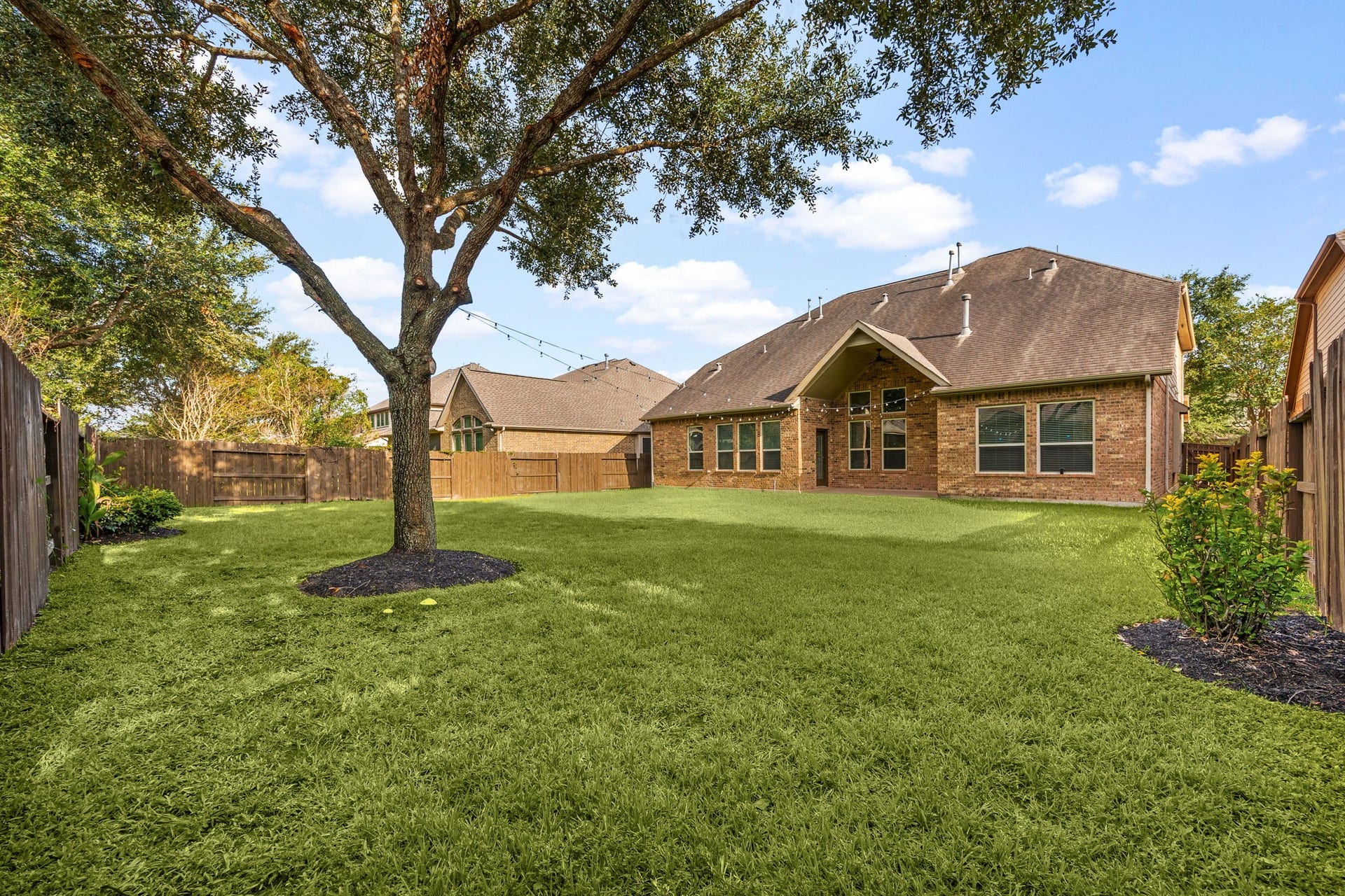 9931 Hutton Park Drive, Katy, TX 77494 This alternative daytime view showcases the sprawling, lush green lawn framed by a fully enclosed privacy fence. A mature, majestic shade tree anchors the yard with pristine landscaping beds, highlighting the deep, versatile footprint of the property and its exceptional potential for creating a private outdoor oasis.