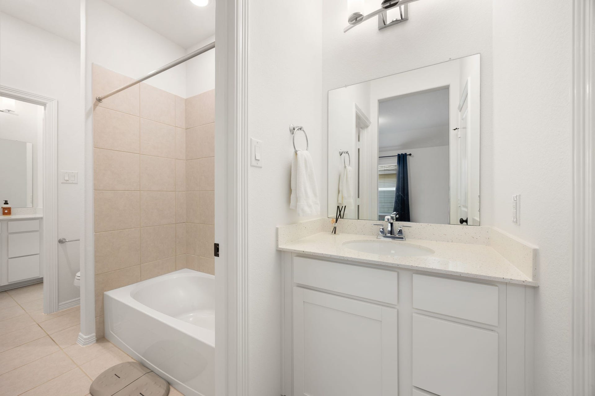 30715 Parkside Passage Drive, Fulshear, TX 77441 This perspective beautifully illustrates the intelligent Hollywood bathroom design, maximizing privacy and functionality for the upper level. Each secondary bedroom enjoys its own private vanity station equipped with storage cabinetry, a solid-surface countertop, and a large mirror under contemporary lighting. These separate dressing alcoves flank a shared central wet room that houses a full tub-and-shower combination lined with clean, neutral ceramic tiling, a toilet area, and low-maintenance tile flooring