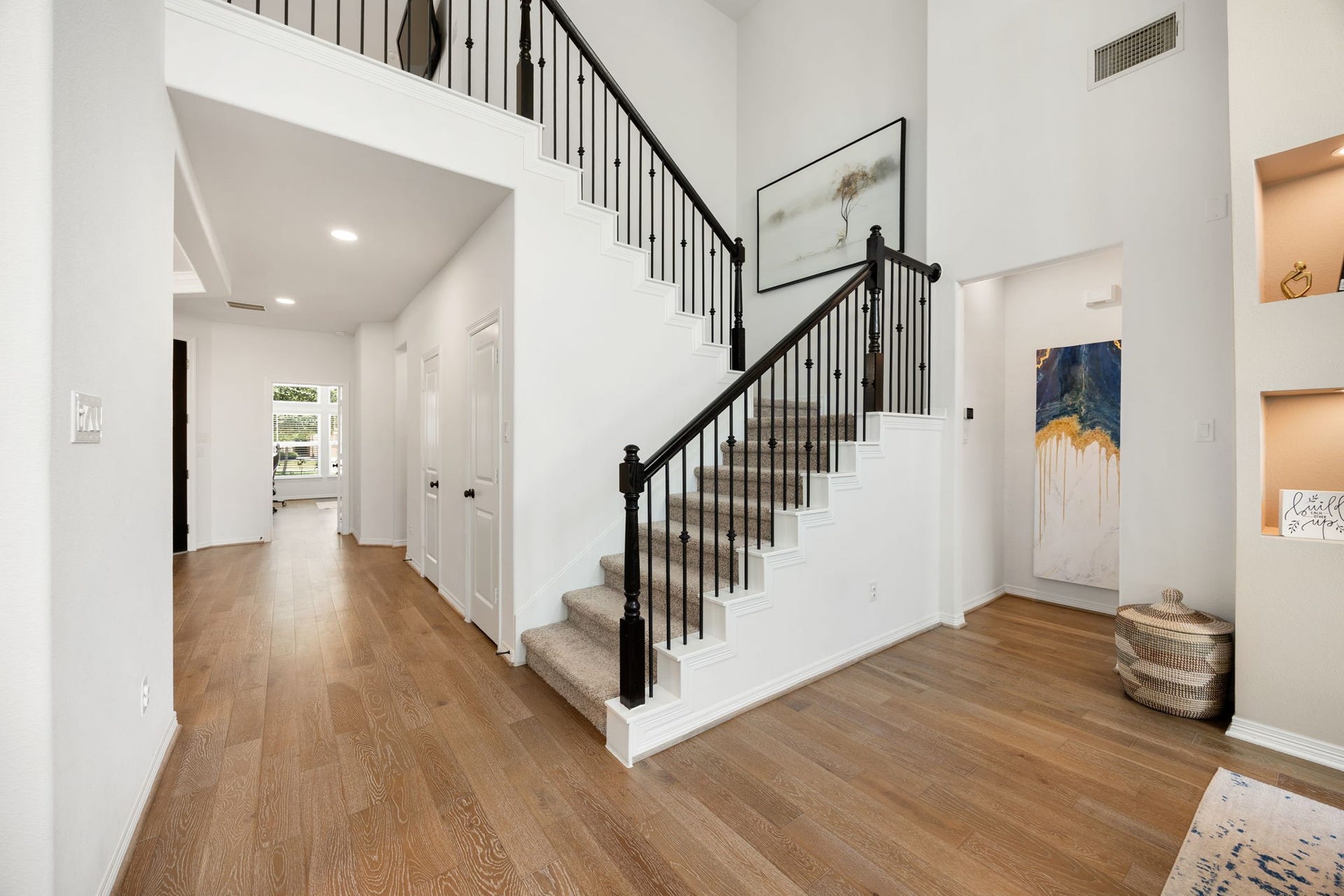 30715 Parkside Passage Drive, Fulshear, TX 77441 A beautifully crafted, sweeping staircase serves as a major architectural feature of the main level, showcasing plush neutral carpeting, rich dark wood handrails, and elegant black wrought-iron balusters. The staircase design gracefully frames the home's open transitions, ascending toward a dramatic second-story catwalk that overlooks the main living pavilion.