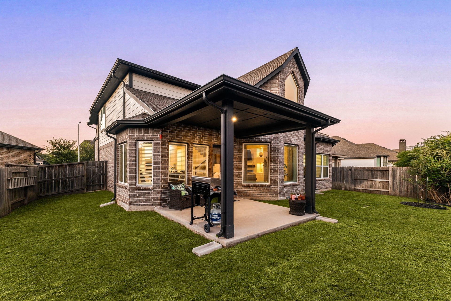 30715 Parkside Passage Drive, Fulshear, TX 77441 An alternate angle of the expansive backyard showcases the impressive scale of the covered patio pavilion and the home's striking rear architecture. The substantial covered structure features deep-toned columns, dark trim, and integrated lighting over a wide concrete base, offering a highly functional space for outdoor living. A fully fenced lawn provides ultimate privacy.