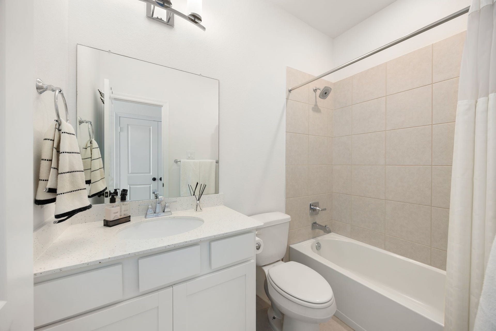 30715 Parkside Passage Drive, Fulshear, TX 77441 This pristine guest en-suite bathroom offers a bright and functional layout featuring a clean white vanity with ample under-sink storage and a neutral quartz countertop. The tub-and-shower combination is lined with classic neutral ceramic tiling, creating a low-maintenance and timeless space for guests.