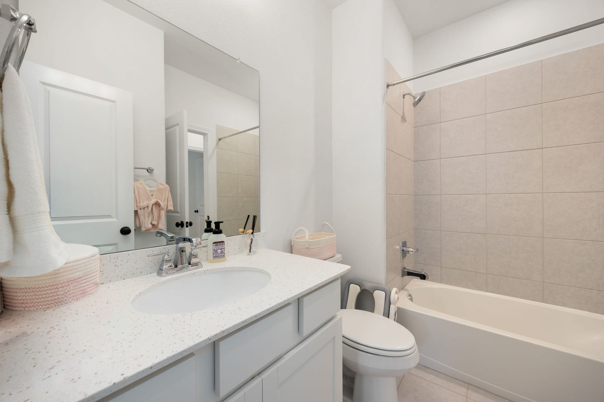 30715 Parkside Passage Drive, Fulshear, TX 77441 This pristine secondary bathroom offers a highly functional layout featuring a generous single vanity with crisp white cabinetry, countertop with undermount sink and mirror. The space includes a comfortable tub-and-shower combination lined with clean, neutral-toned ceramic tile surrounds, all grounded by low-maintenance flooring that matches the home's cohesive design.