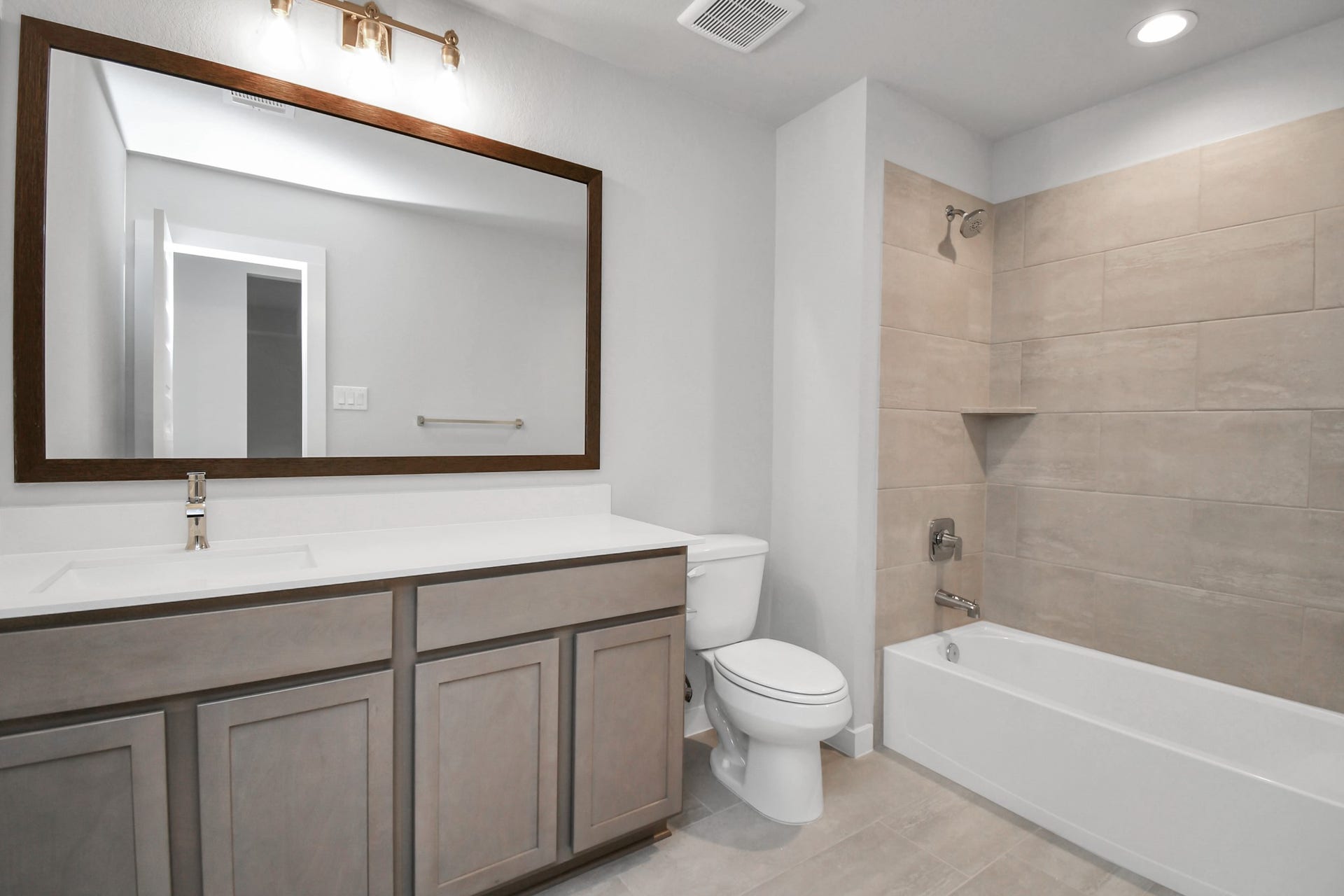 Secondary bath features tile flooring, bath/shower combo with tile surround, light stained wood cabinets, beautiful light countertop. Sample photo of completed home with similar floor plan. Actual colors and selections may vary.