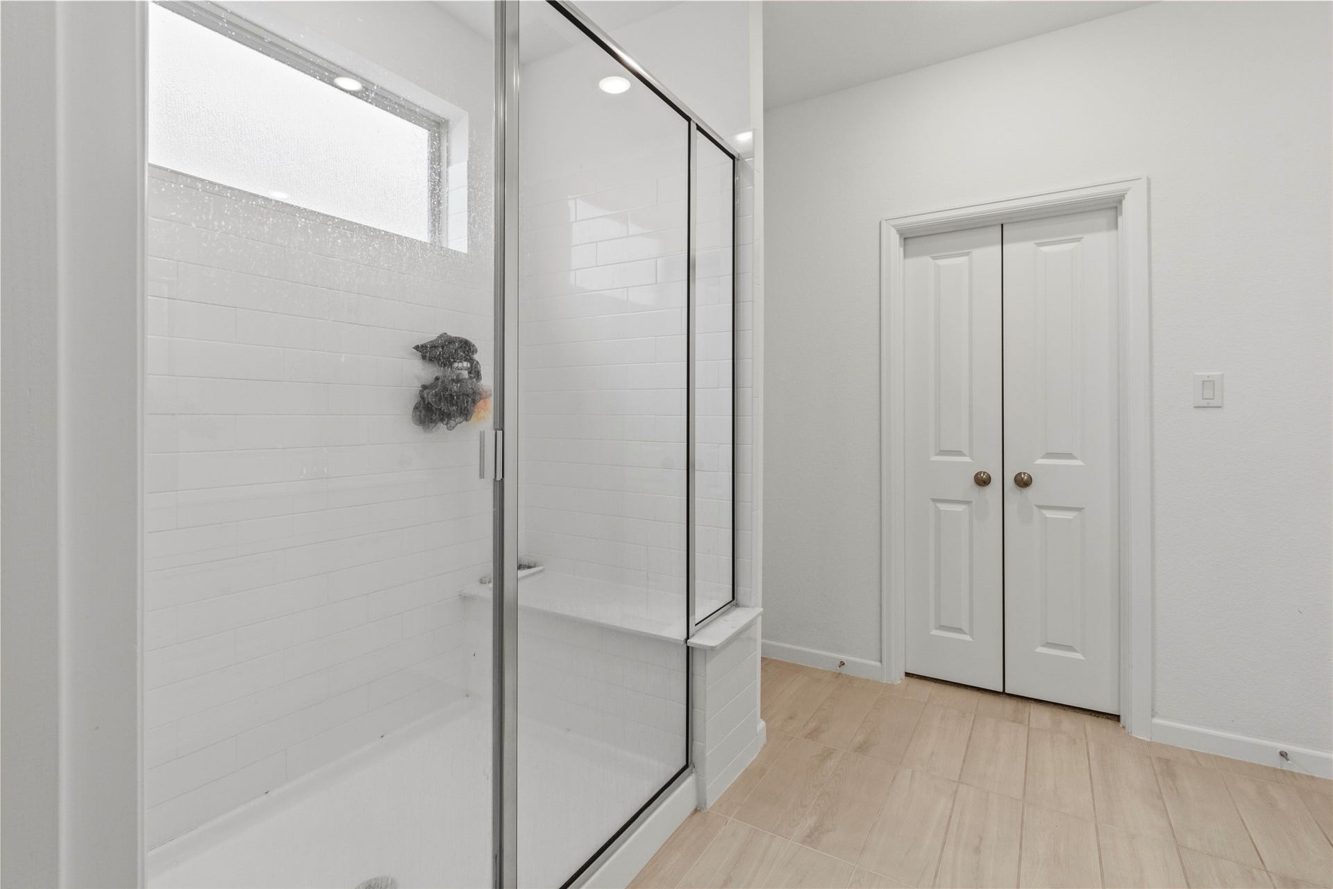 2909 Ballast Green Drive, La Marque, TX 77568 Sleek and modern bathroom off the primary with elegant white tiles, complemented by stylish wood-look flooring and convenient double doors for storage.