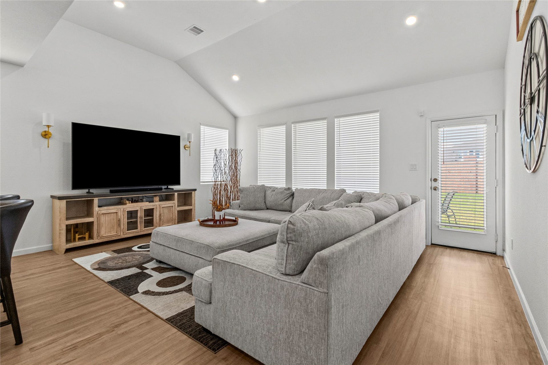 2909 Ballast Green Drive, La Marque, TX 77568 Bright and inviting living area with vaulted ceilings features a spacious sectional sofa, large windows with blinds for natural light, and a modern entertainment setup. A door leads to a backyard space, enhancing indoor-outdoor living.