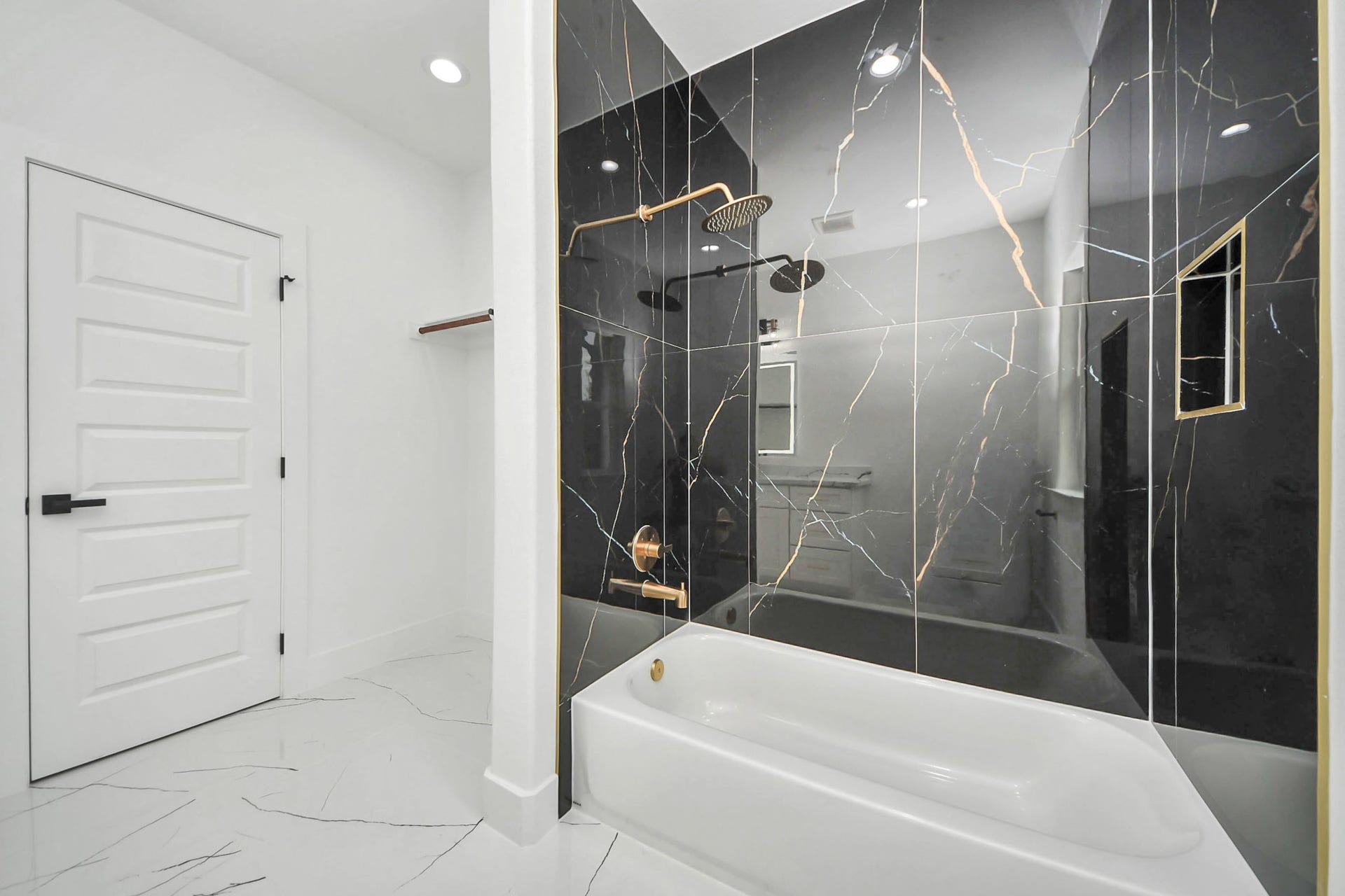 6711 Crestmont Street, Houston, TX 77033 Luxurious bathroom featuring sleek black marble tiles with gold veining, a modern rainfall showerhead, and a pristine white bathtub, set against elegant white walls and flooring.