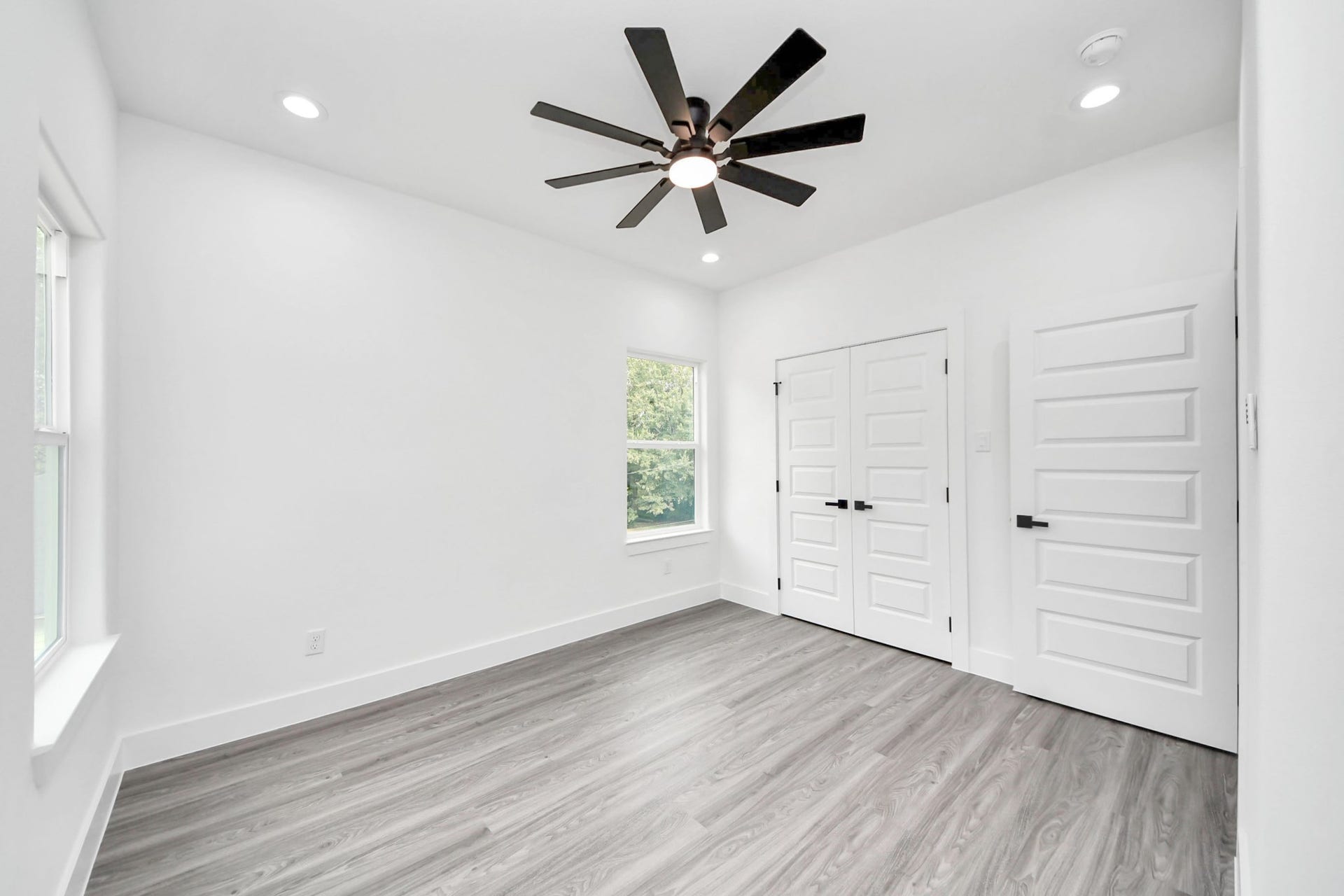 6711 Crestmont Street, Houston, TX 77033 Bright and airy bedroom featuring modern wood flooring, a sleek ceiling fan, and ample natural light from large windows, creating a welcoming atmosphere.