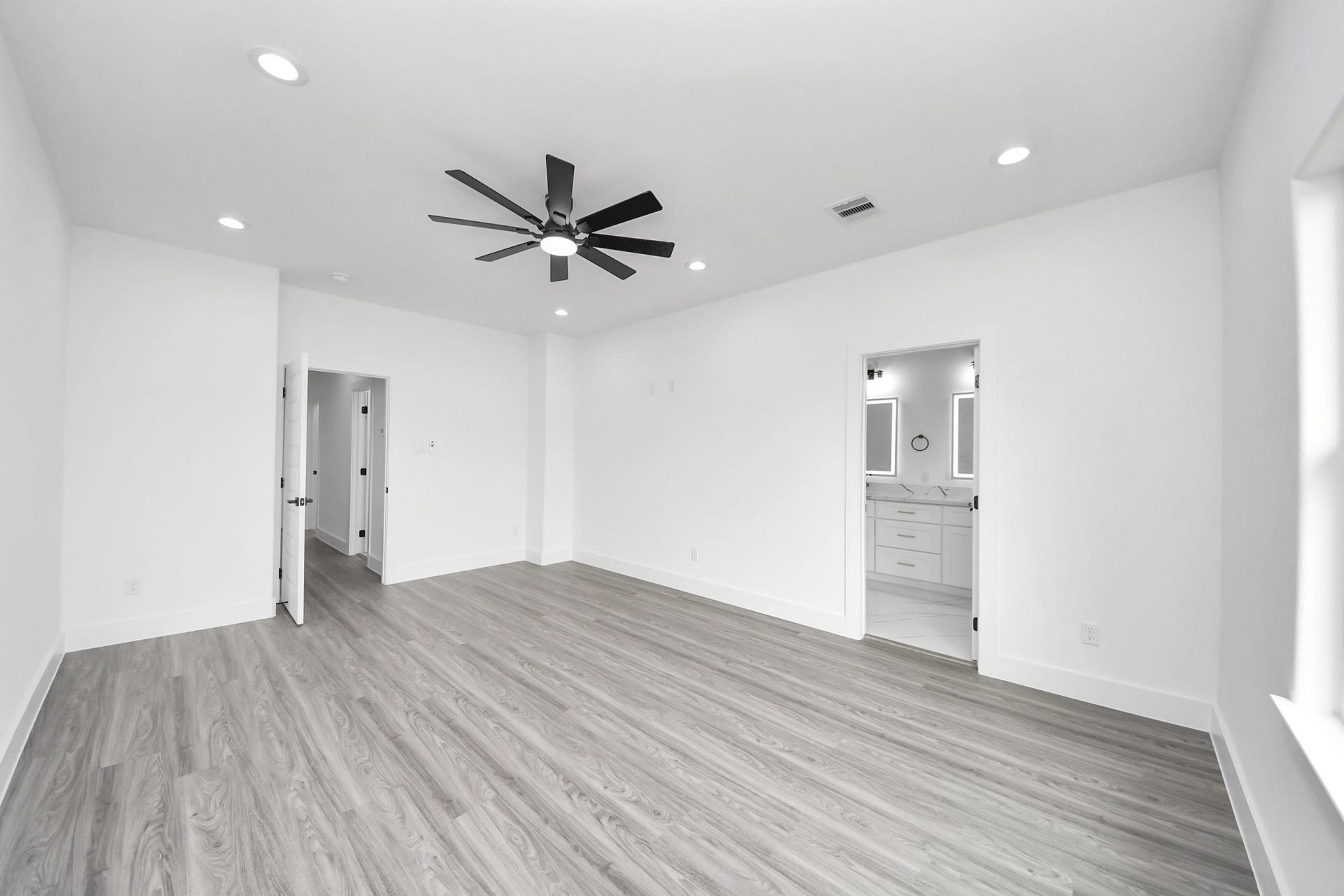 6711 Crestmont Street, Houston, TX 77033 Spacious, modern room featuring sleek wood flooring, recessed lighting, and a ceiling fan, with direct access to a bright, stylish bathroom.