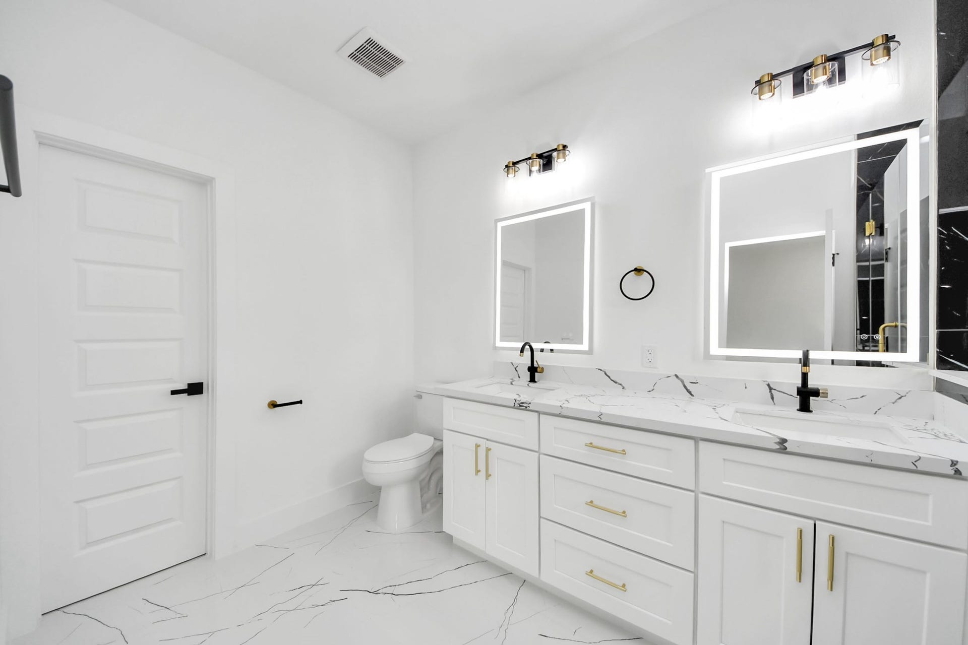 6711 Crestmont Street, Houston, TX 77033 Sleek and modern bathroom featuring dual sinks with elegant marble countertops, illuminated mirrors, and stylish black fixtures.