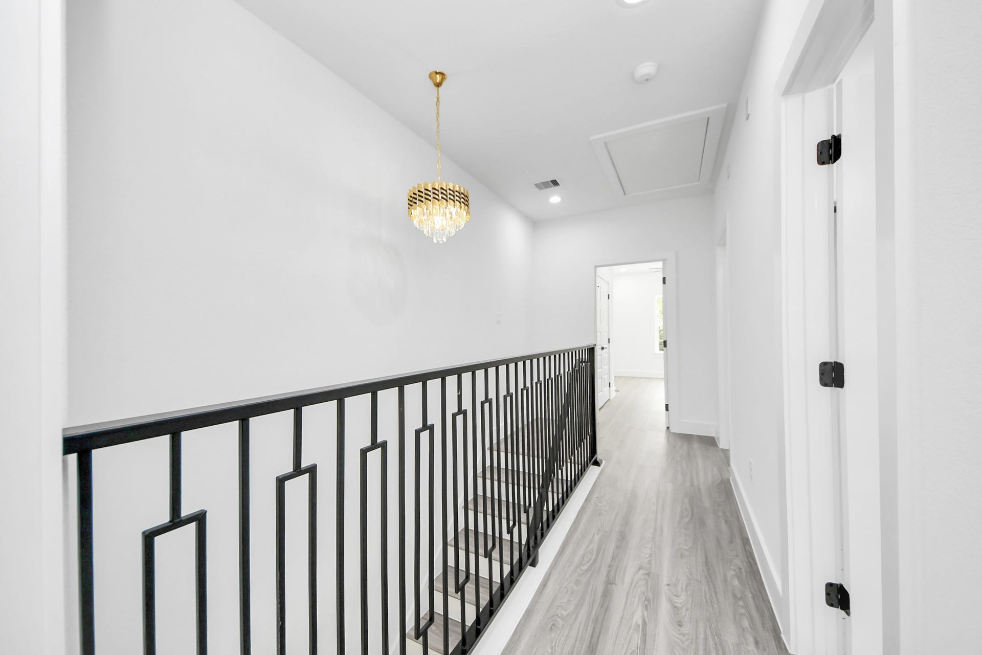 6711 Crestmont Street, Houston, TX 77033 Elegant hallway featuring modern railing, a stylish chandelier, and sleek wood flooring, leading to bright rooms.