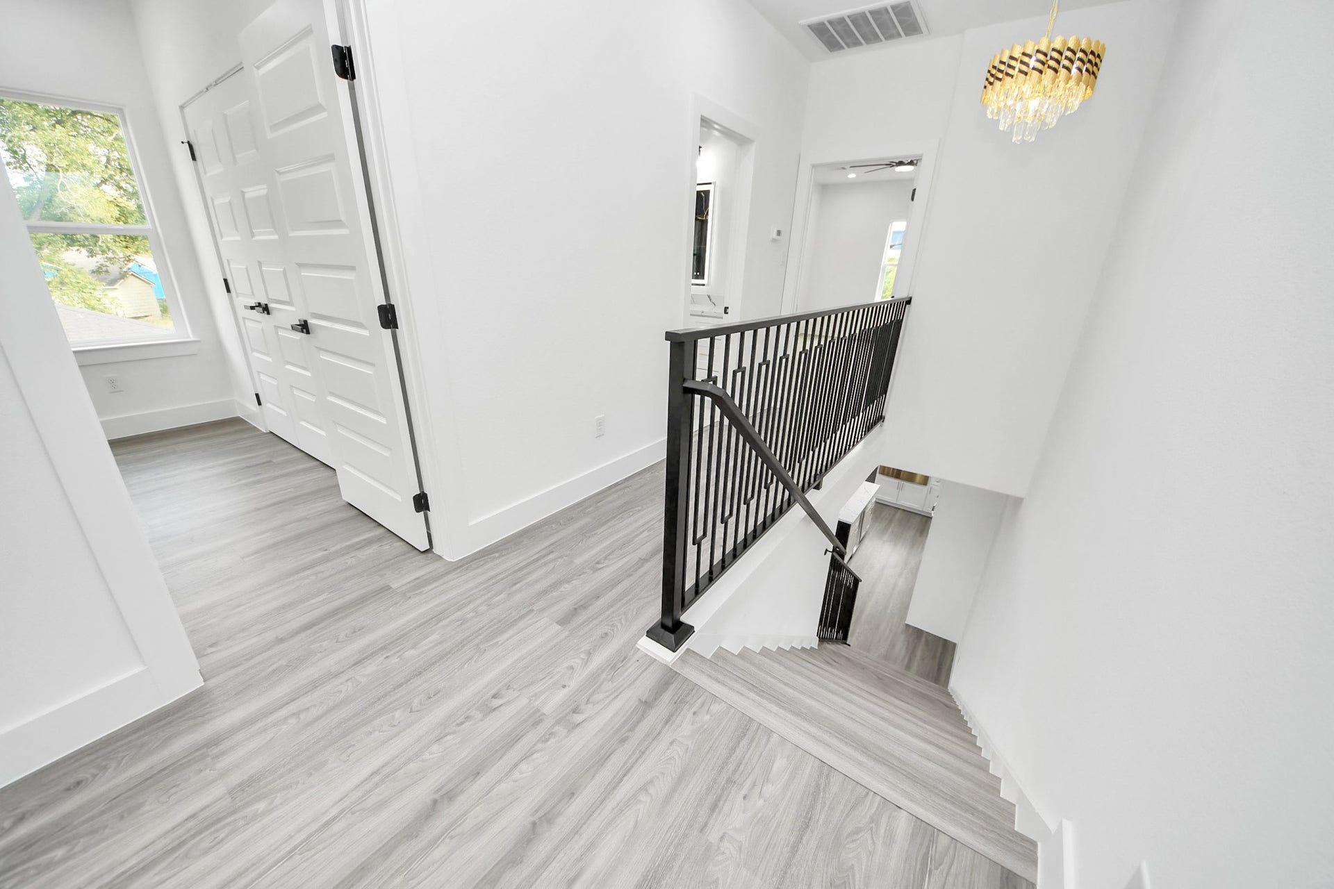 6711 Crestmont Street, Houston, TX 77033 Bright and modern hallway with sleek wood flooring, elegant black railing, and a chic chandelier accentuating the airy space.