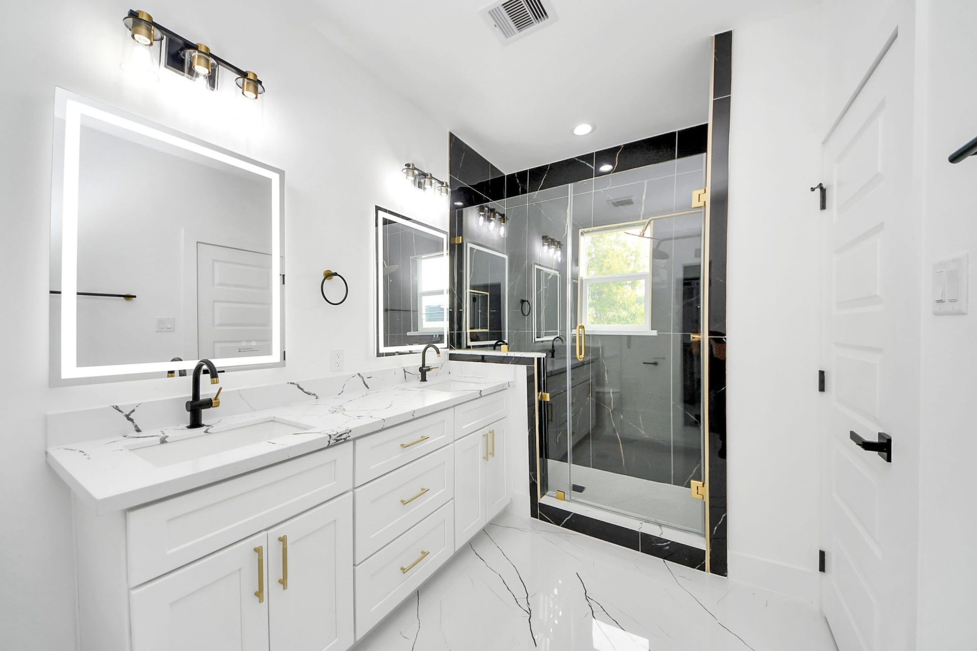 6711 Crestmont Street, Houston, TX 77033 Luxurious bathroom featuring a spacious dual-sink vanity with elegant marble countertops, sleek black fixtures, and a stylish glass-enclosed shower accented with gold hardware.
