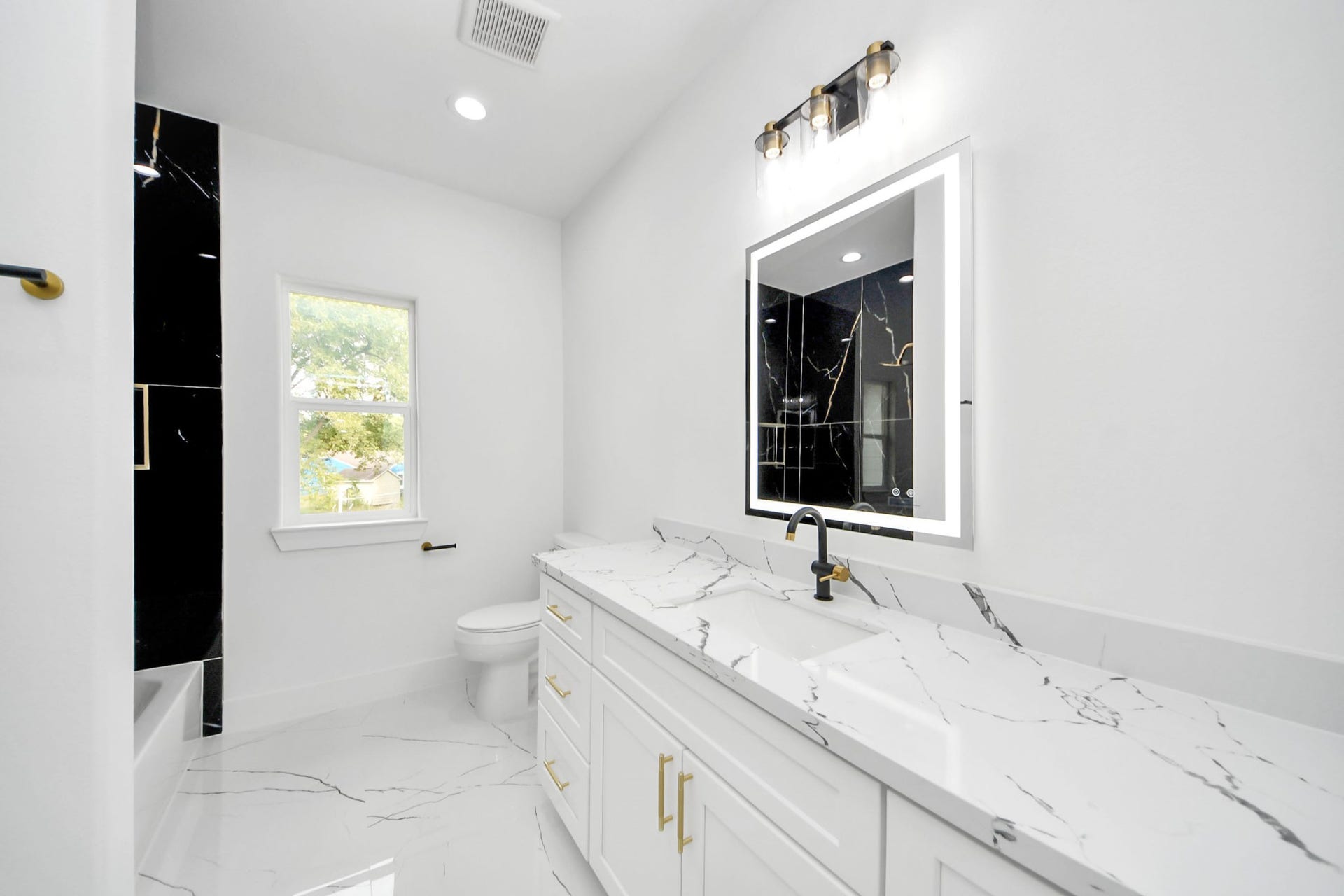 6711 Crestmont Street, Houston, TX 77033 Elegant bathroom featuring a sleek, marble-topped vanity with modern fixtures, complemented by a stylish illuminated mirror and luxurious black accent wall.