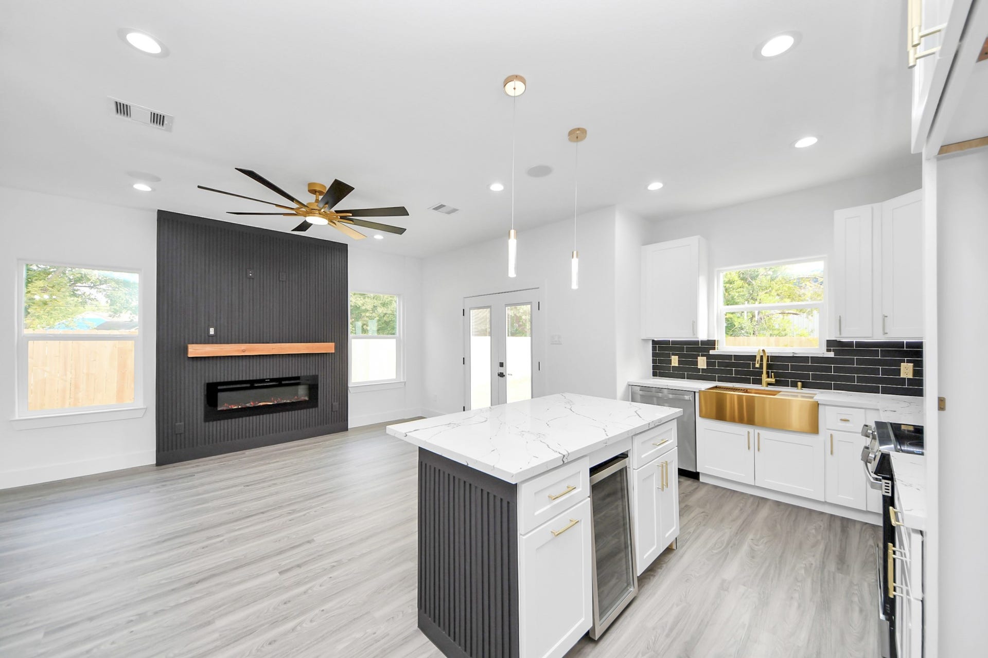 6711 Crestmont Street, Houston, TX 77033 Experience modern elegance in this open-concept living space featuring a sleek kitchen with a large island, gold accents, and a striking black backsplash. The adjacent living area offers a contemporary fireplace and stylish ceiling fan, all enhanced by abundant natural light.